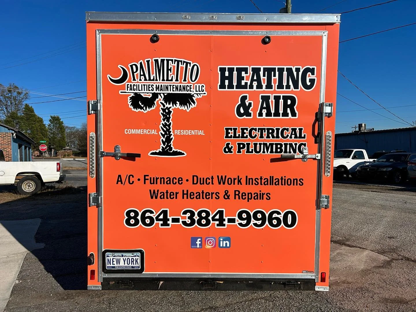 Orange service trailer advertising heating, air conditioning, electrical, and plumbing services including duct work, water heaters, and repairs, with a phone number and social media icons, parked on a street.