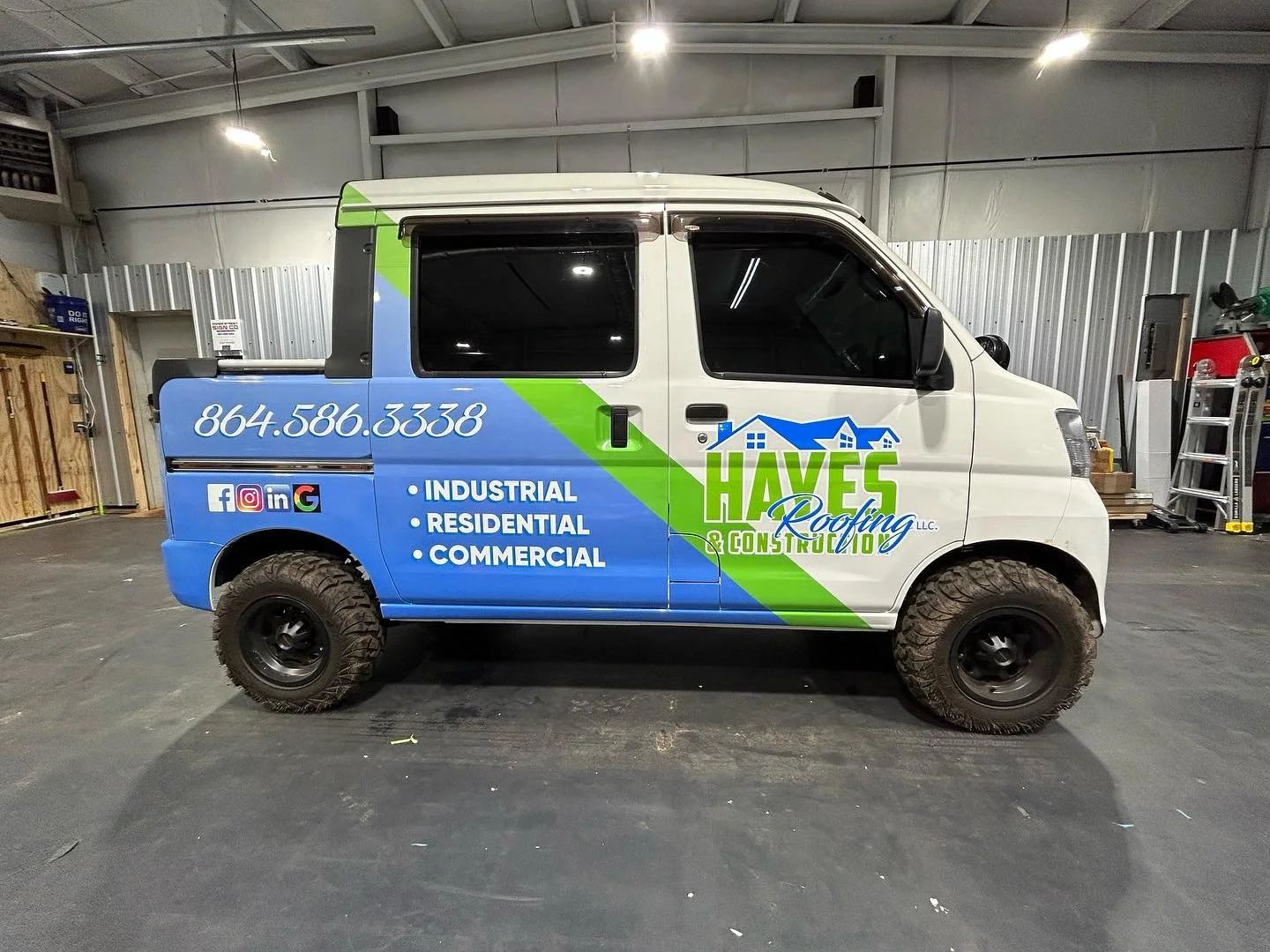 A small commercial van inside a warehouse with a RTV, displaying branding for Haves Roofing & Construction LLC, including a phone number, social media icons, and services like industrial, residential, and commercial roofing.