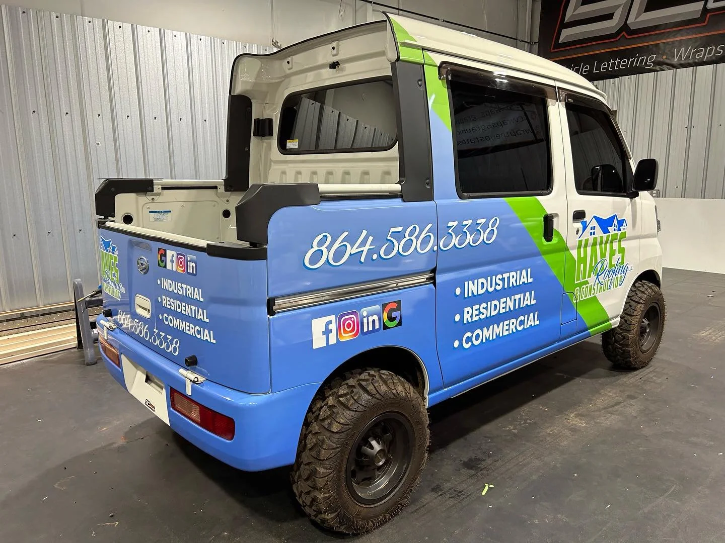 A small electric utility vehicle with advertising for HAVES Roofing Construction, featuring contact phone number and social media icons, parked indoors against a metal wall.