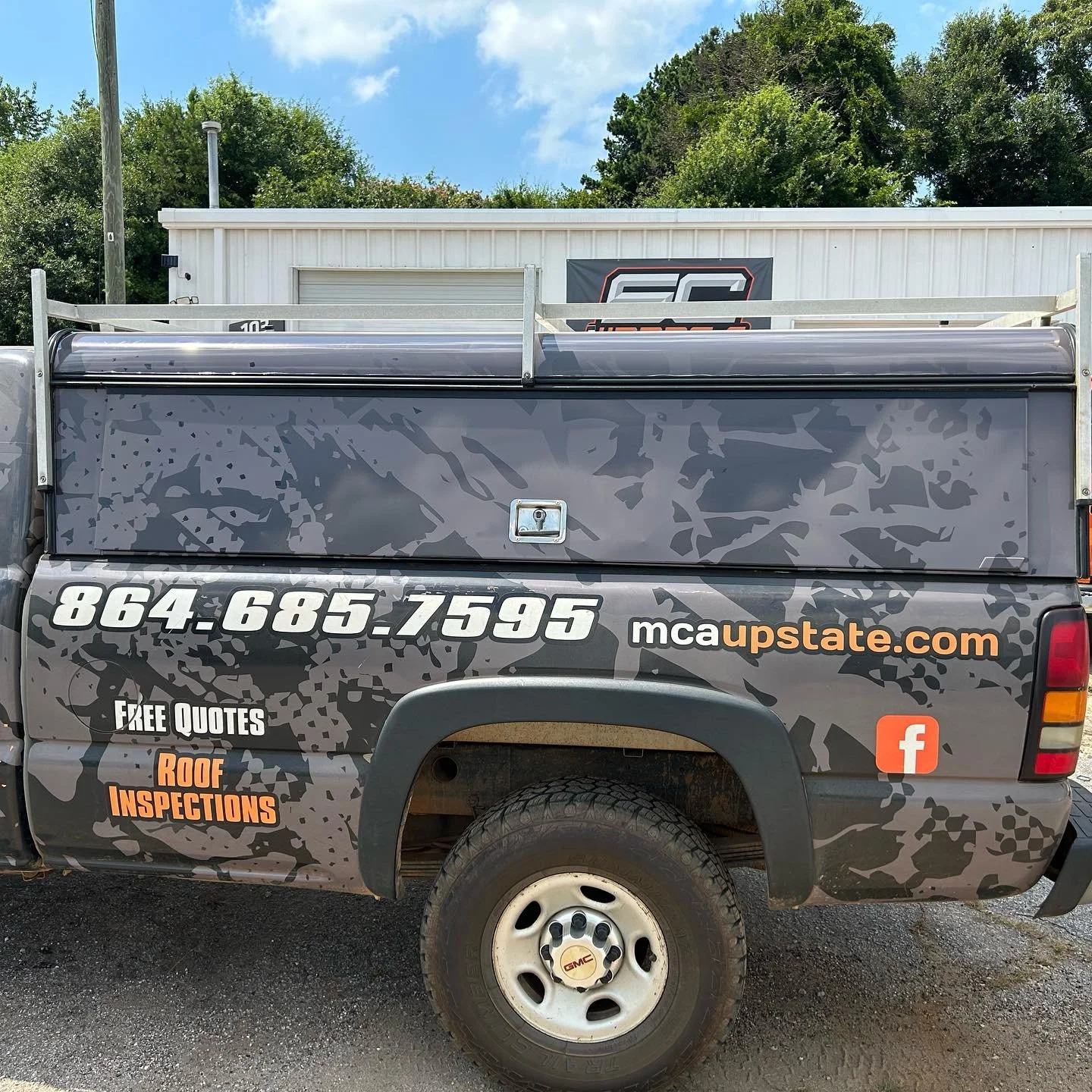 Side view of a black pickup truck with advertisement graphics, including a phone number, website, Facebook icon, and text promoting roof inspections and free quotes.