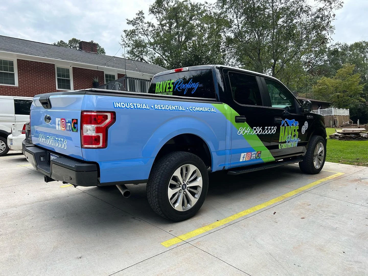 A pickup truck with a custom wrap advertising Haves Roofing LLC, parked in a parking lot. The truck is black and blue with green accents, displaying the company name, contact number, and services including industrial, residential, and commercial roof