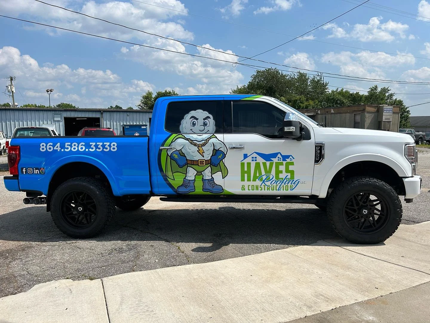 Company truck with a cartoon superhero mascot, blue and white color scheme, and the words "HAVEF Roofing & Construction LLC" on the side, parked on a paved lot under a partly cloudy sky.
