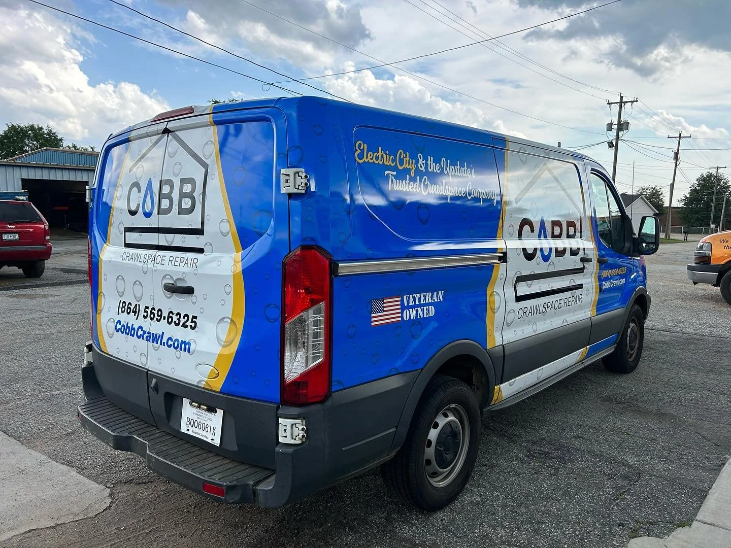 A Cobb Crawlspace Repair company van parked in a parking lot, featuring blue, white, and yellow branding with contact information, veteran-owned badge, and company slogan.