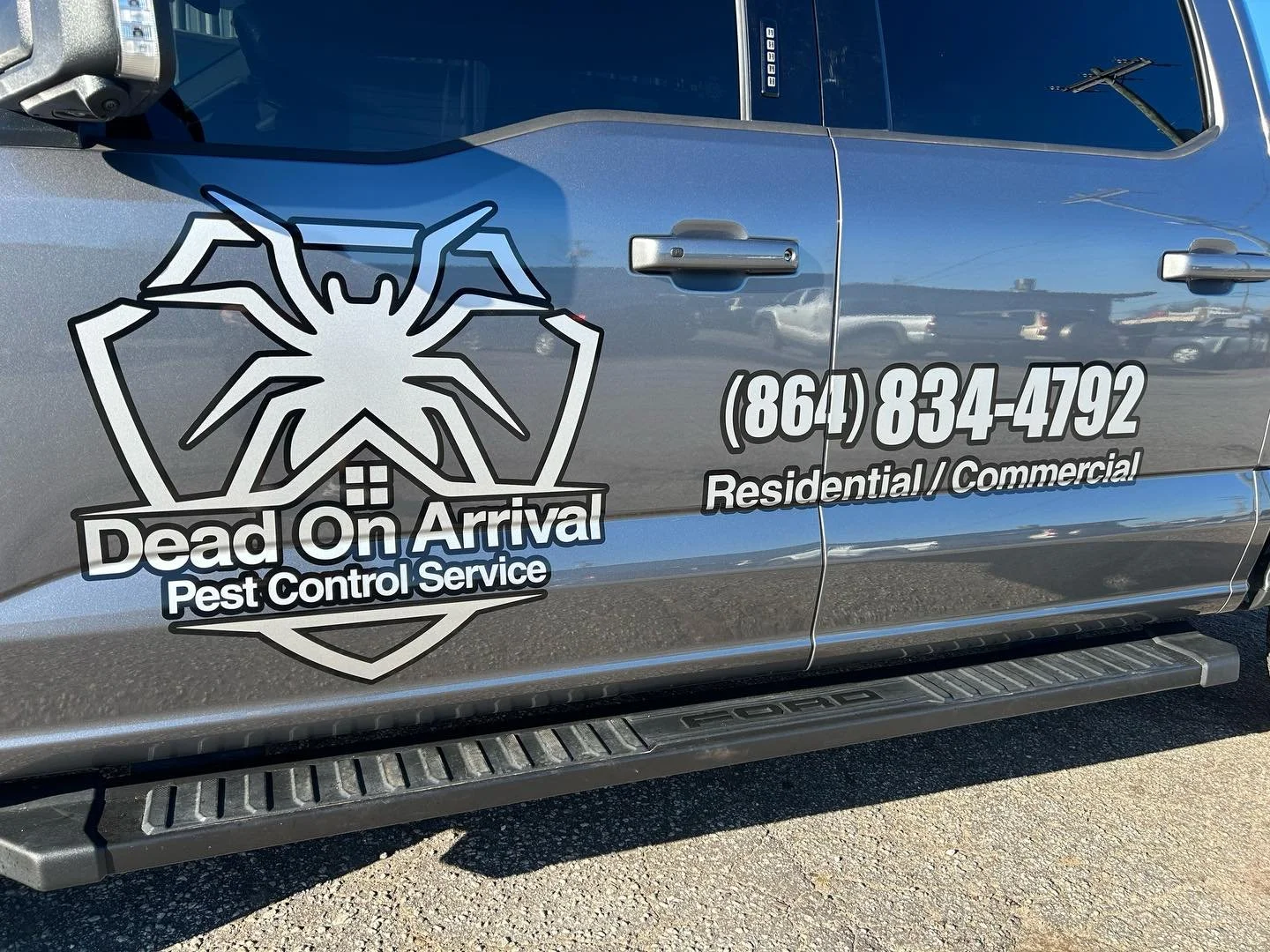 Side of a truck with company logo and contact information for pest control service, featuring a spider emblem, and phone number 864-834-4792.