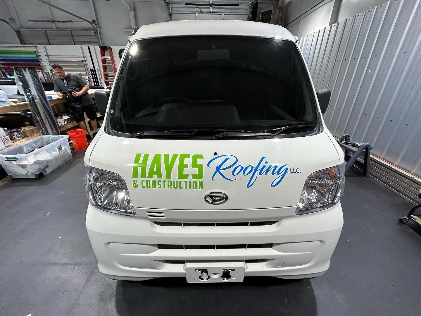 White commercial van with company logo reading 'HAYES Roofing & Construction LLC' parked indoors in a workshop or garage.