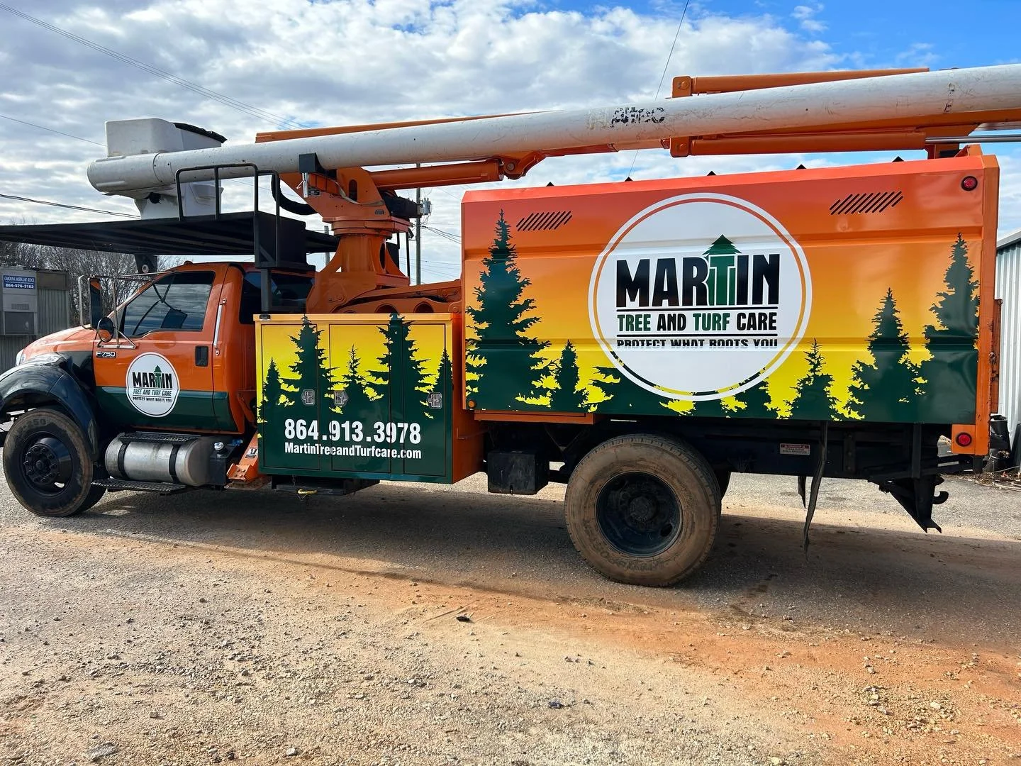A service truck with Martin Tree and Turf Care advertisement featuring pine trees and contact info, parked on a dirt surface under a partly cloudy sky.