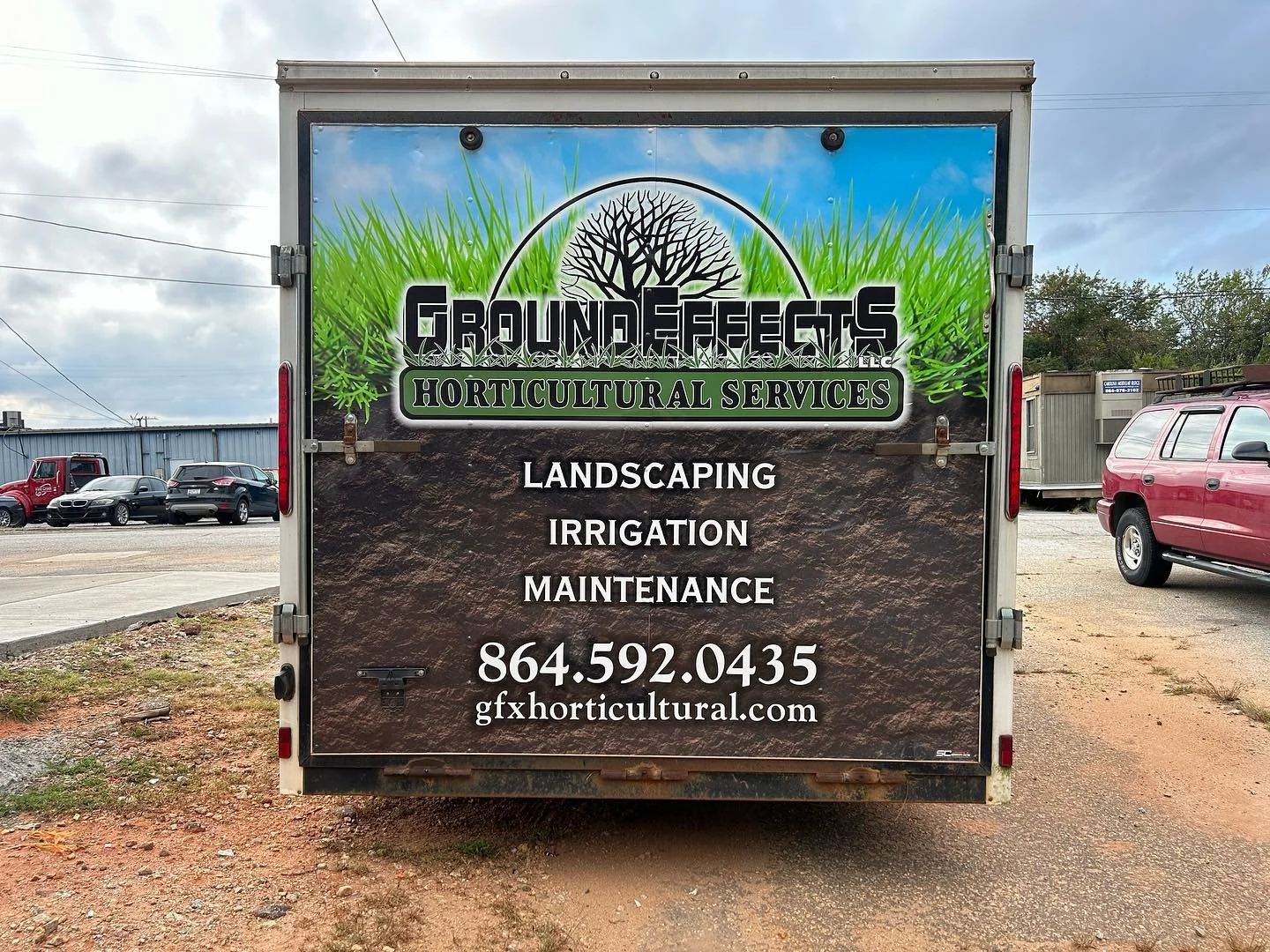 Sign for Ground Effects Horticultural Services advertising landscaping, irrigation, and maintenance services, with phone number and website, on the back of a truck parked outdoors.