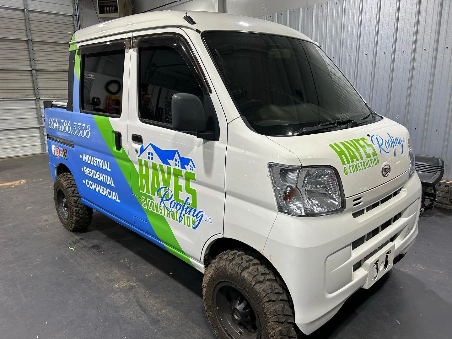A small white van with colorful branding and contact information for Haves Roofing & Construction parked inside a garage or warehouse.