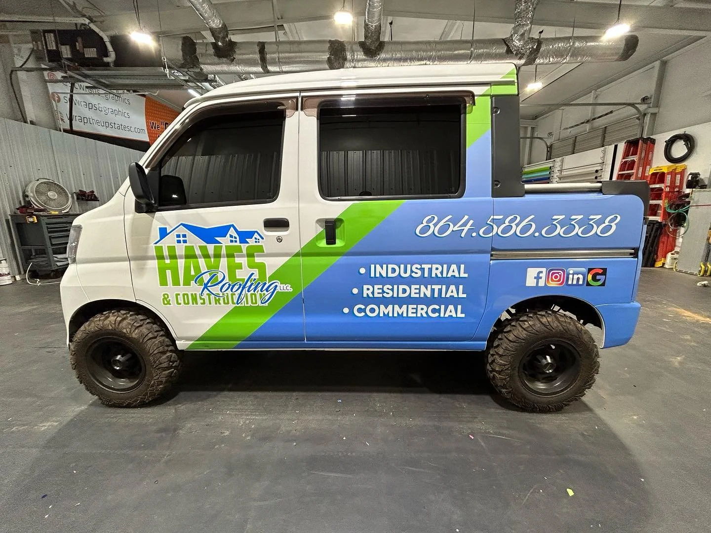 Company truck for Haves Roofing & Construction parked indoors, showcasing the company's logo, contact number, and services including industrial, residential, and commercial roofing, social media icons, and tire details.
