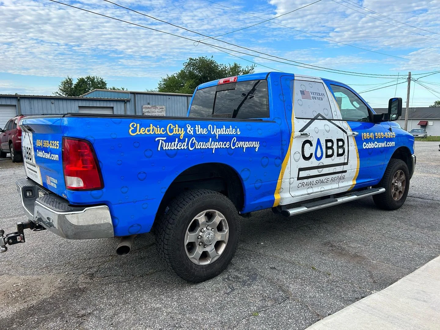 A blue pickup truck with graphics advertising CABB Crawl Space Repair, with contact info and website, parked on a gravel lot under a partly cloudy sky.