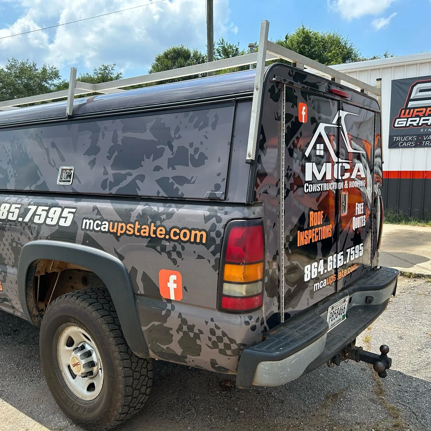 Black pickup truck with advertisement for MCA Construction & Roofing on the side and back, including logos, website, and phone number.