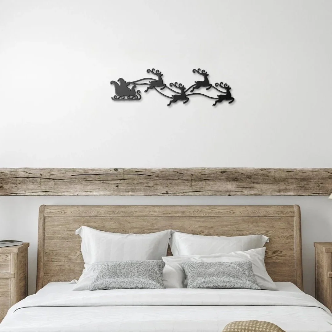 Decorative metal wall art of a reindeer pulling Santa's sleigh, positioned above a wooden headboard in a bedroom.