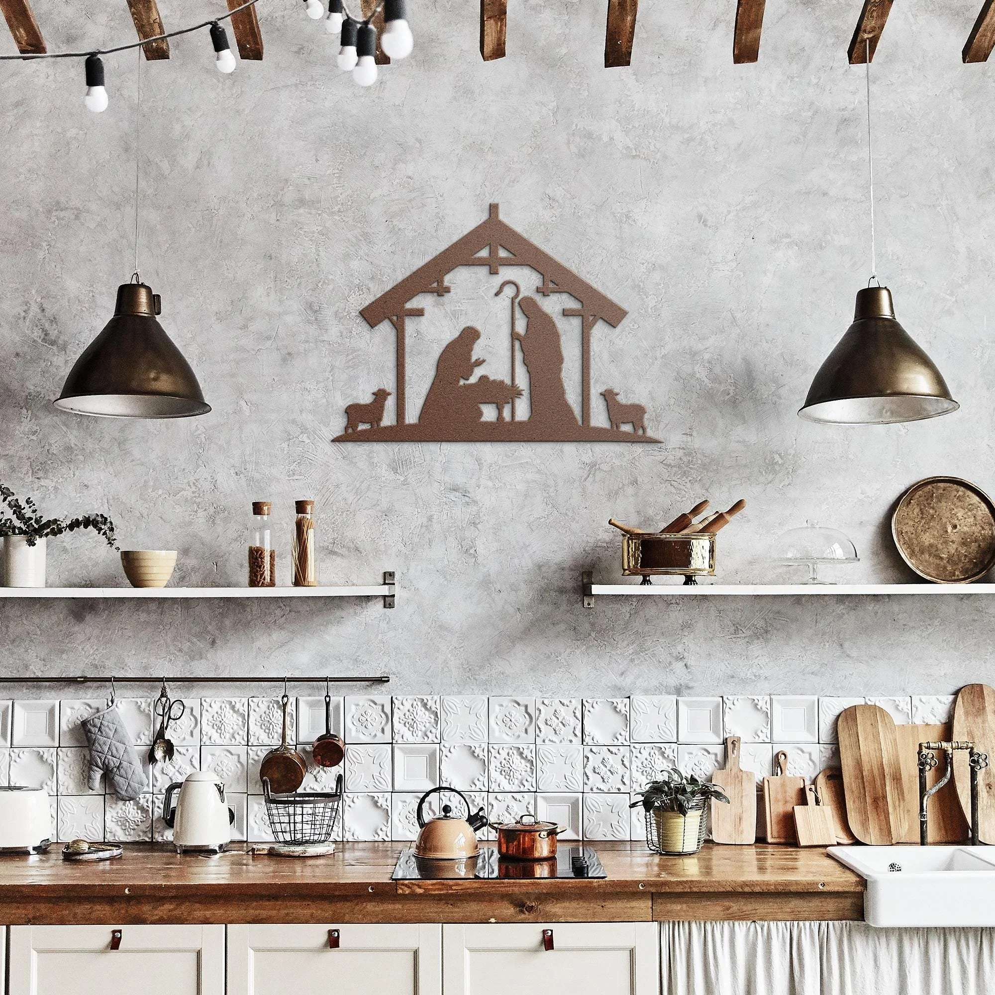 Modern kitchen with wooden countertop, white cabinets, wall in white and gray tones, hanging black lamps, and a metal Nativity scene wall art.