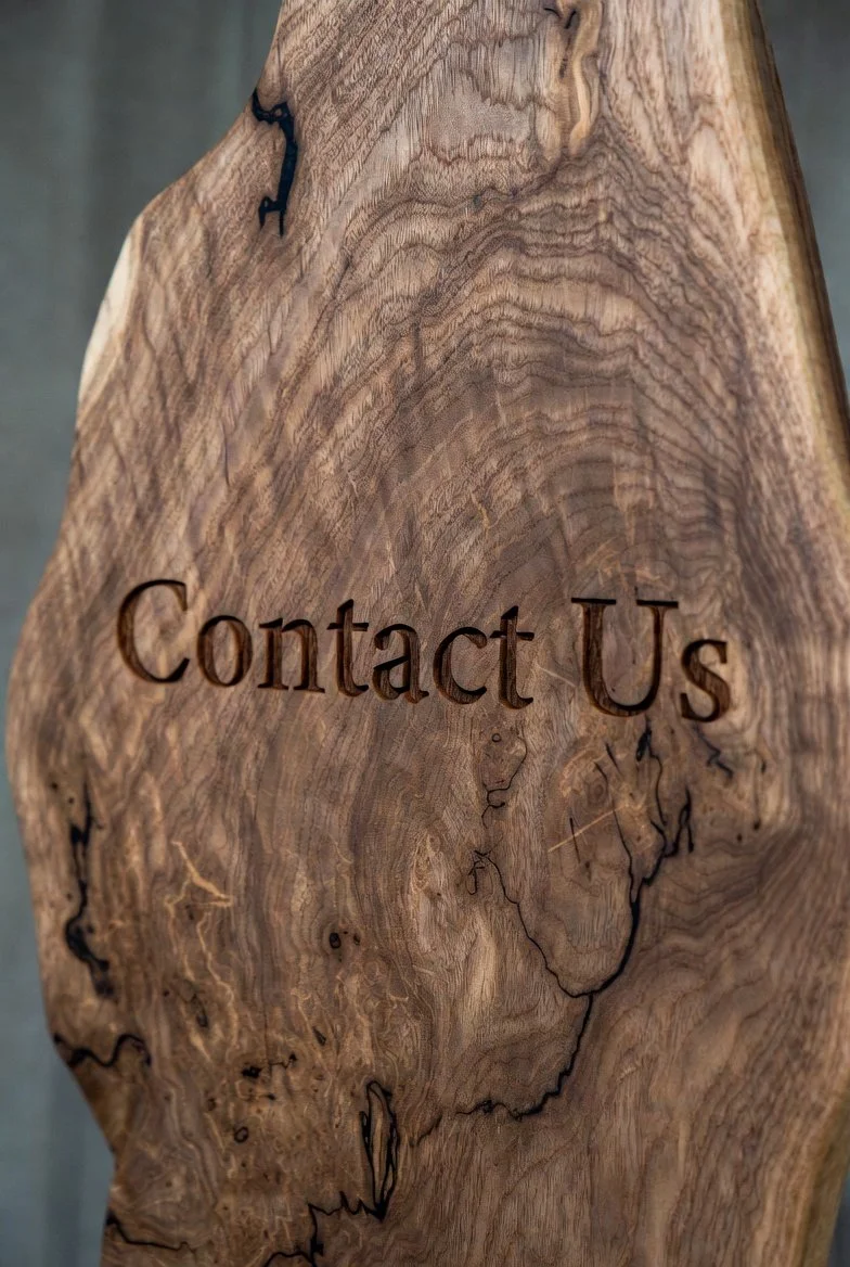 Close-up of a wooden surface with the words "Contact Us" engraved into it.