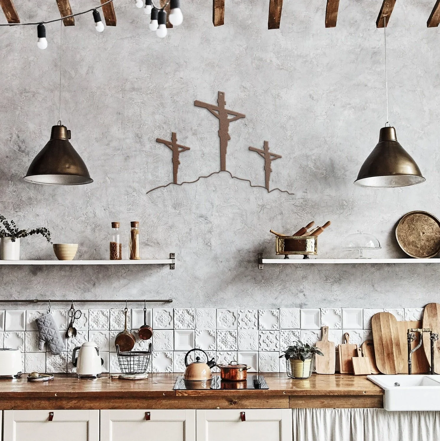 Rustic kitchen with two black pendant lights, white shelving with jars and kitchen tools, a Biblical cross wall art, white tiled backsplash, wooden countertop with kitchen utensils, kettle, potted plant, and a white apron in front of a sink.