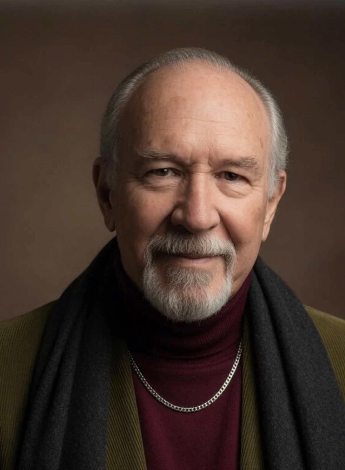 Close-up portrait of an older man with a beard and mustache, wearing a dark scarf and a necklace, against a neutral background.