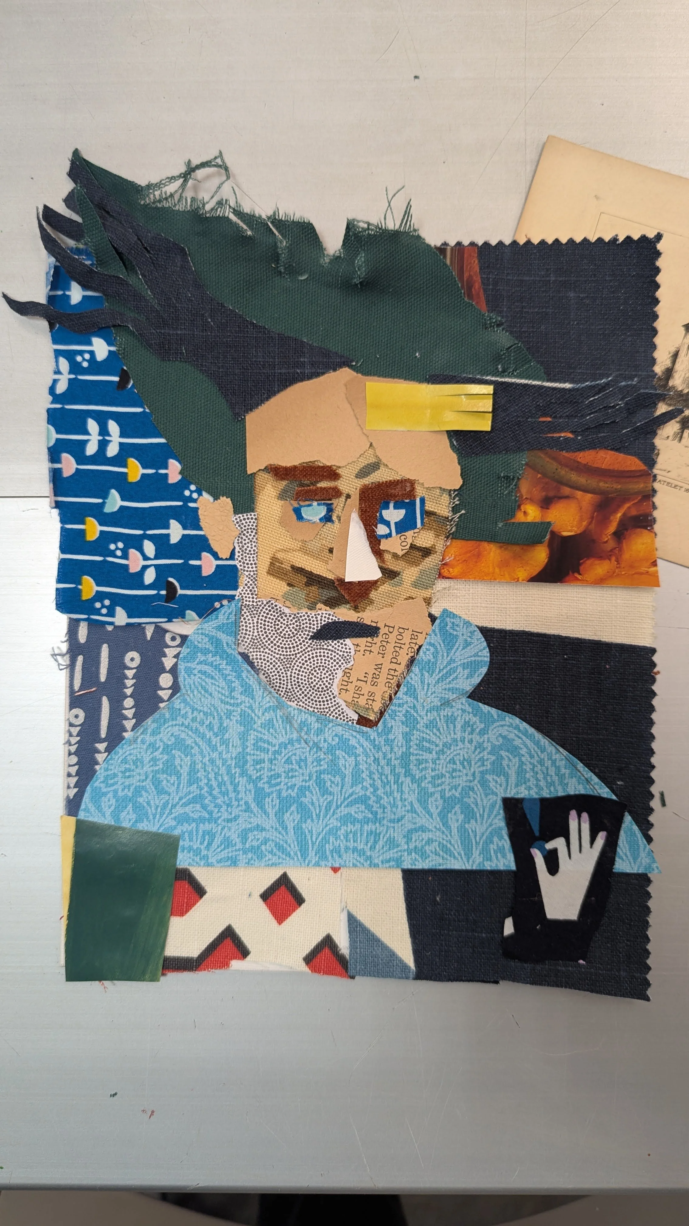 Collage of torn paper pieces forming a collage portrait of a man wearing a blue shirt, with glasses and dark hair.