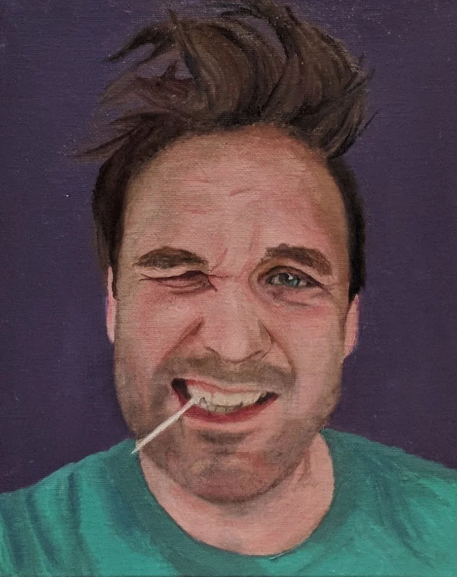 A man with messy brown hair, one eye closed, and a cotton swab in his mouth, smiling at the camera against a purple background.