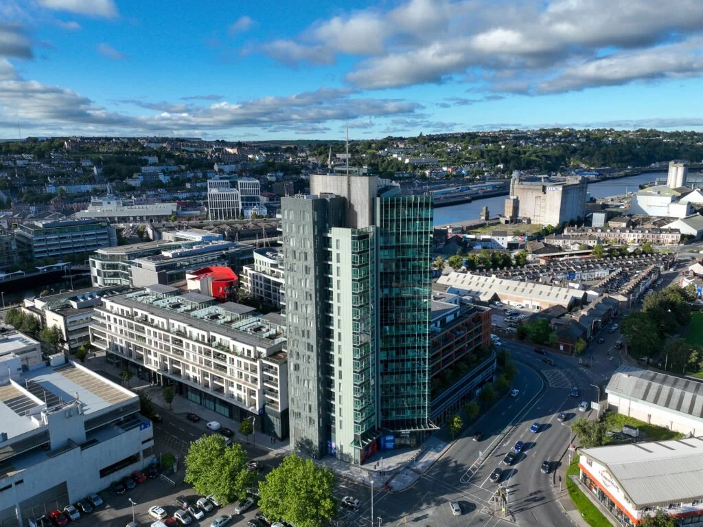 Aerial view of a cityscape showing modern high-rise buildings, a river, and a partly cloudy sky.