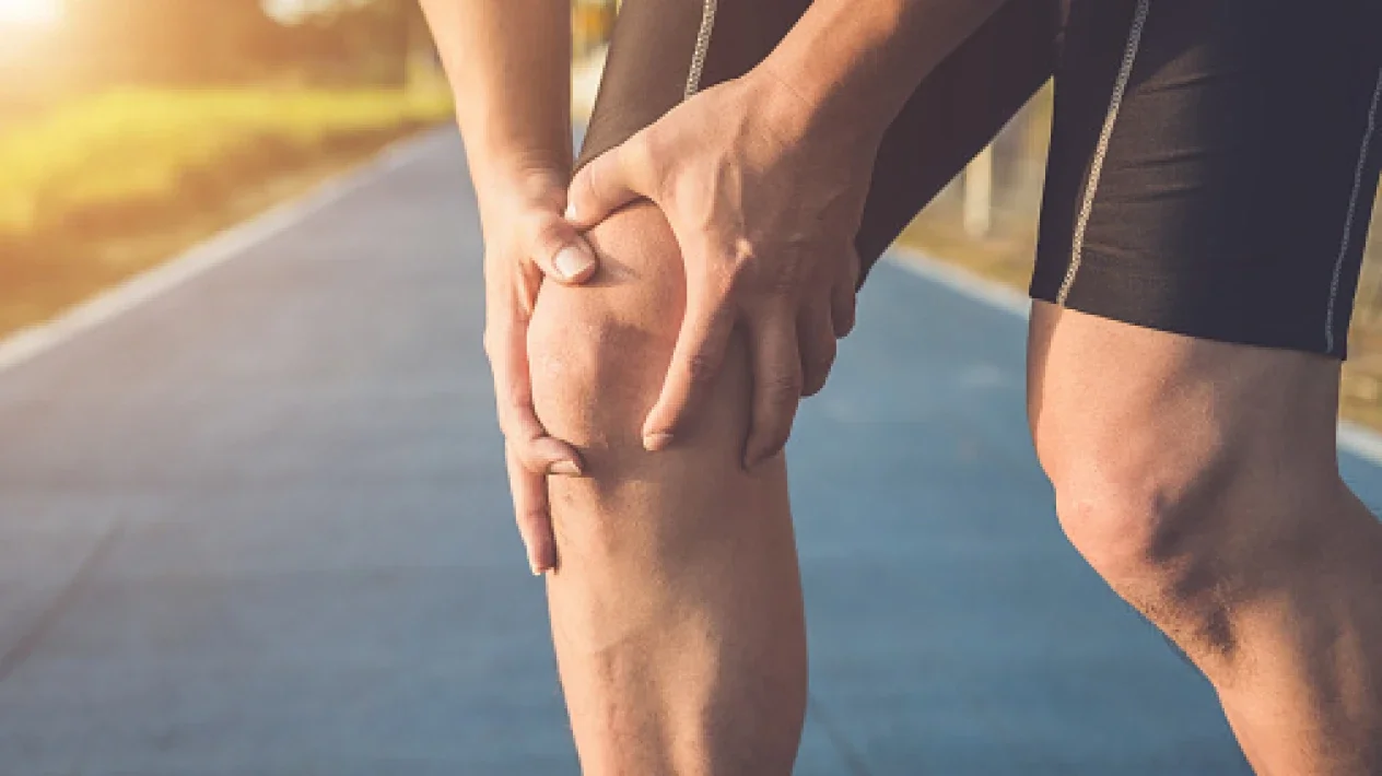 A person is holding their knee in pain while standing on an outdoor running track.