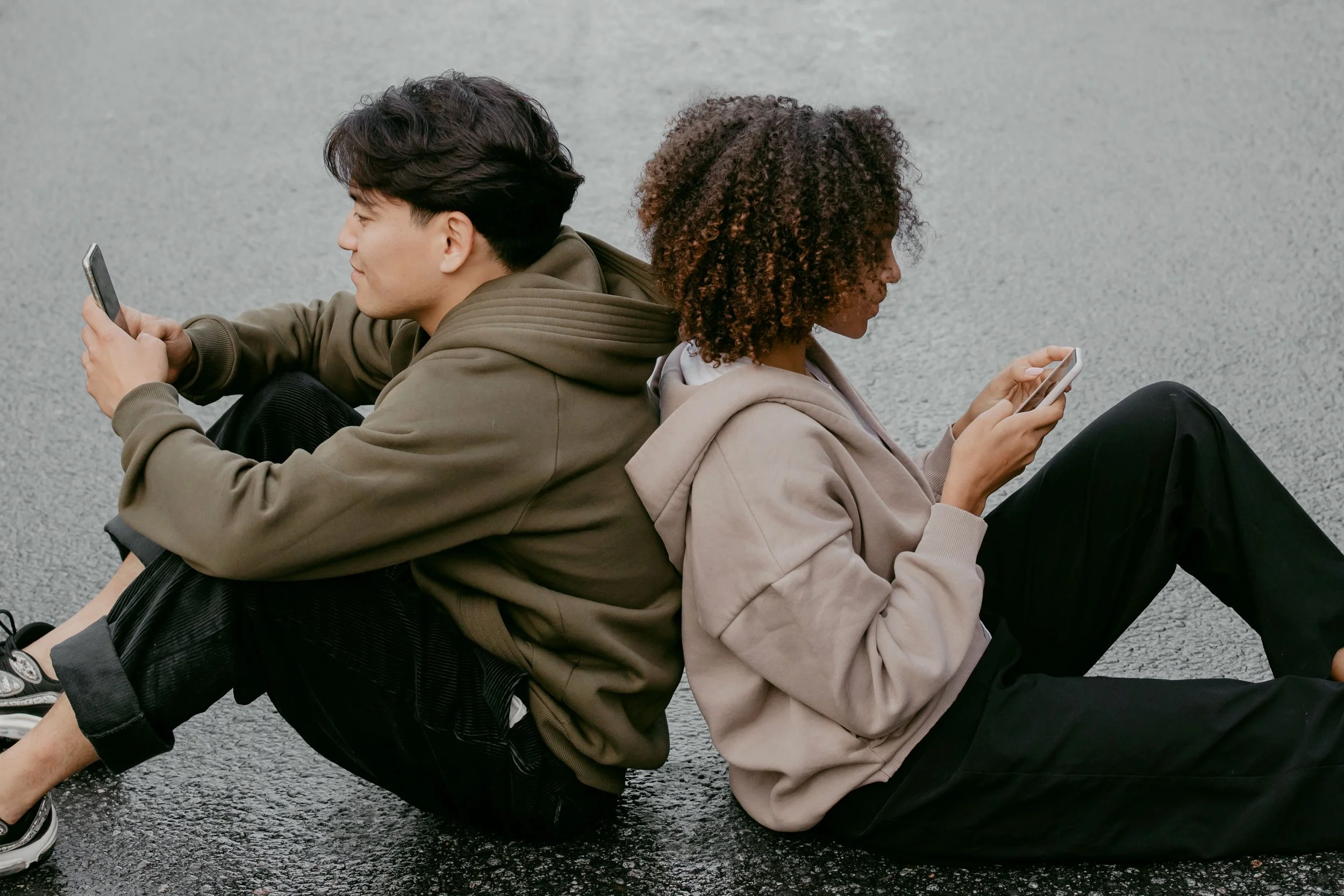 Two teenagers sitting side by side, absorbed in their phones, a common scene discussed in adolescent therapy in Limassol