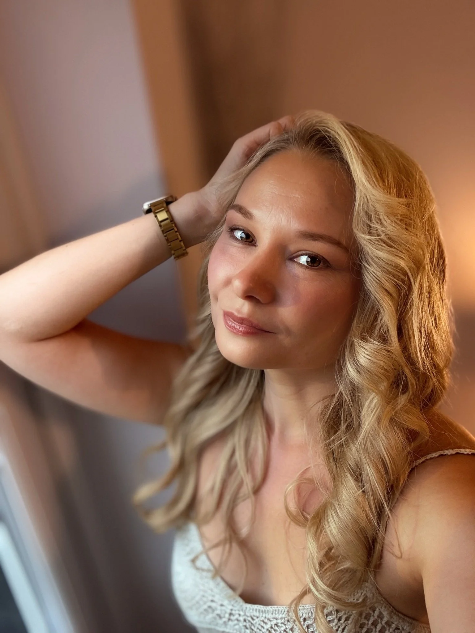 Portrait of Naysha Gane, LinkedIn strategist and coach, wearing a cream top with her hand resting in her hair.