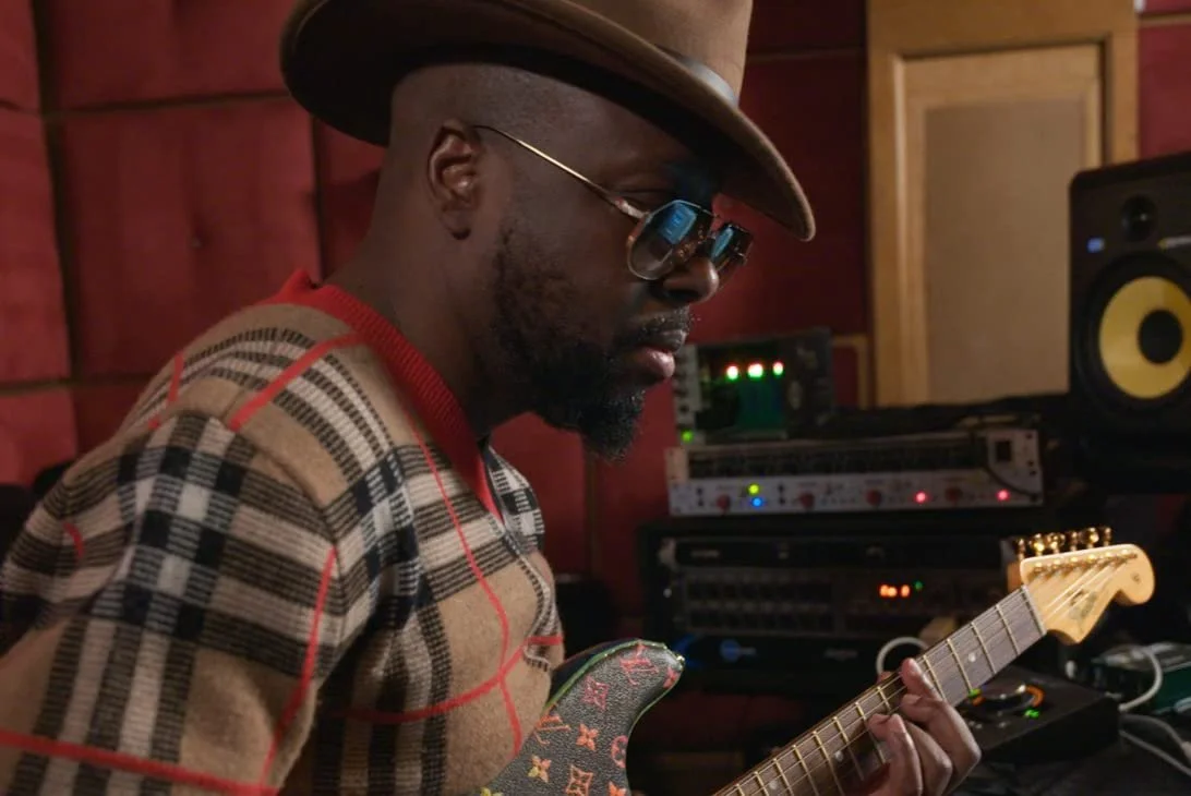 Wyclef Jean, playing an electric guitar in a music studio.