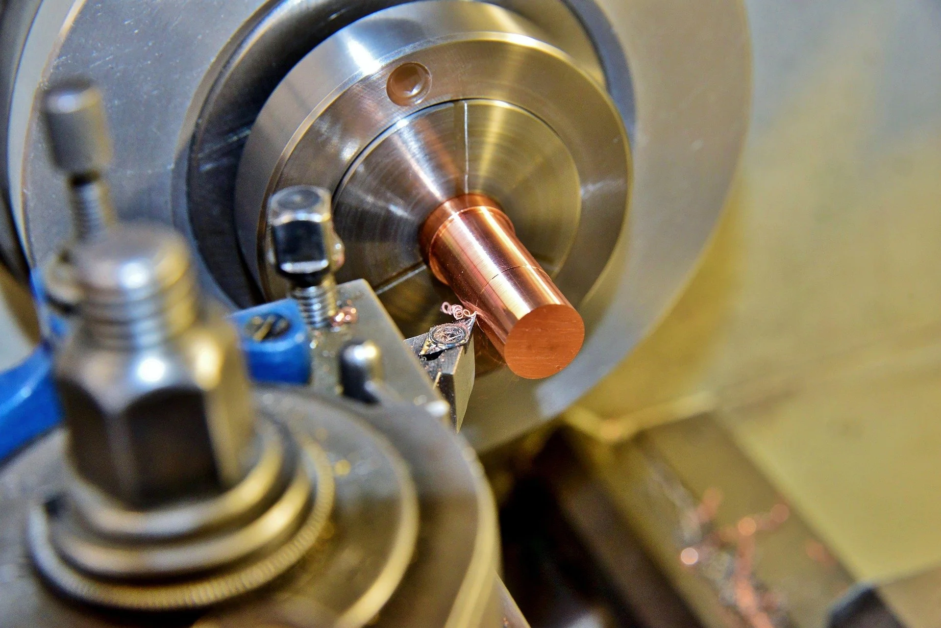 Close-up of a metal lathe machine shaping a copper rod, with metal shavings nearby.