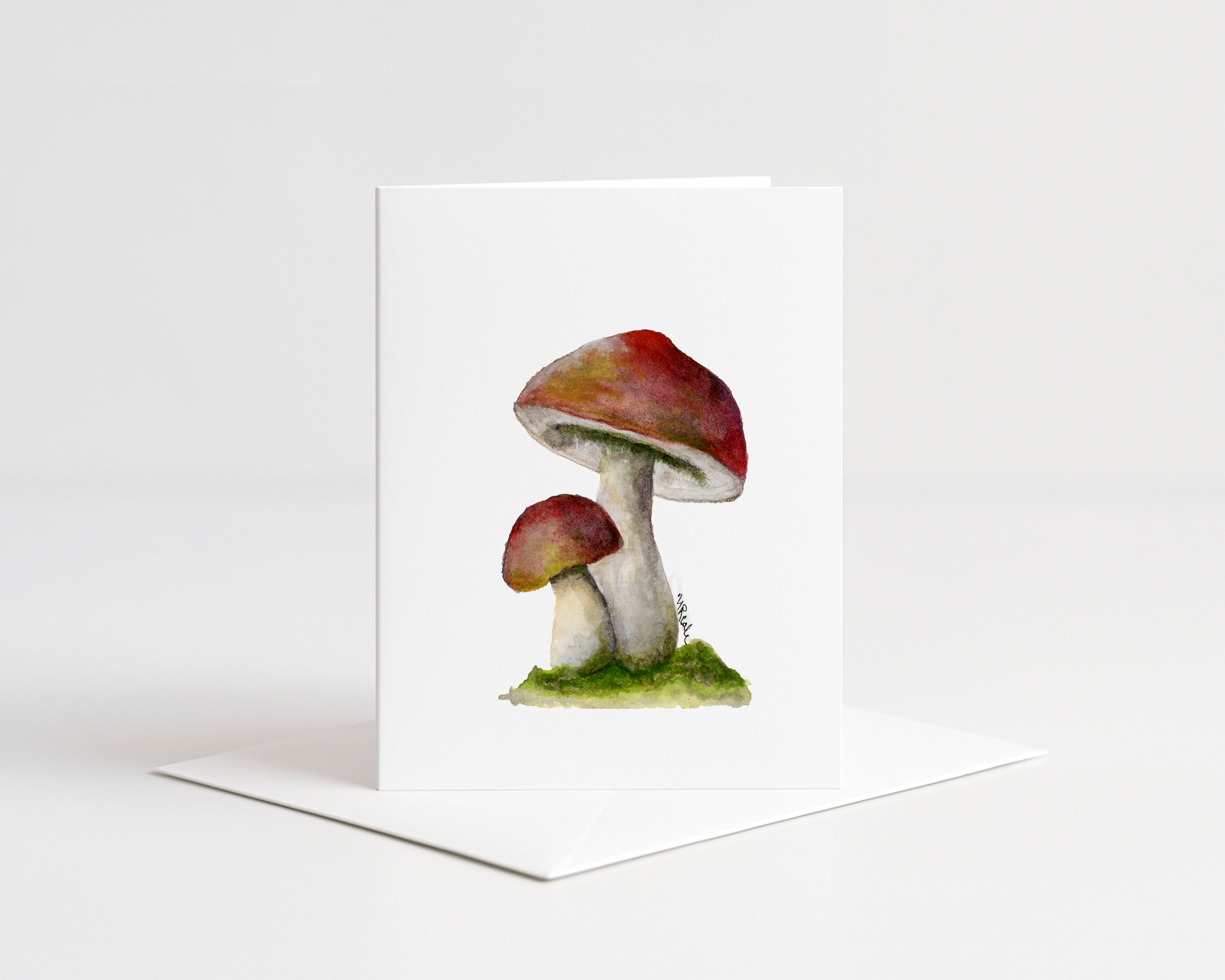 Watercolor painting of three mushrooms with red caps and white stems, set on green moss and grass, on artist's paper.