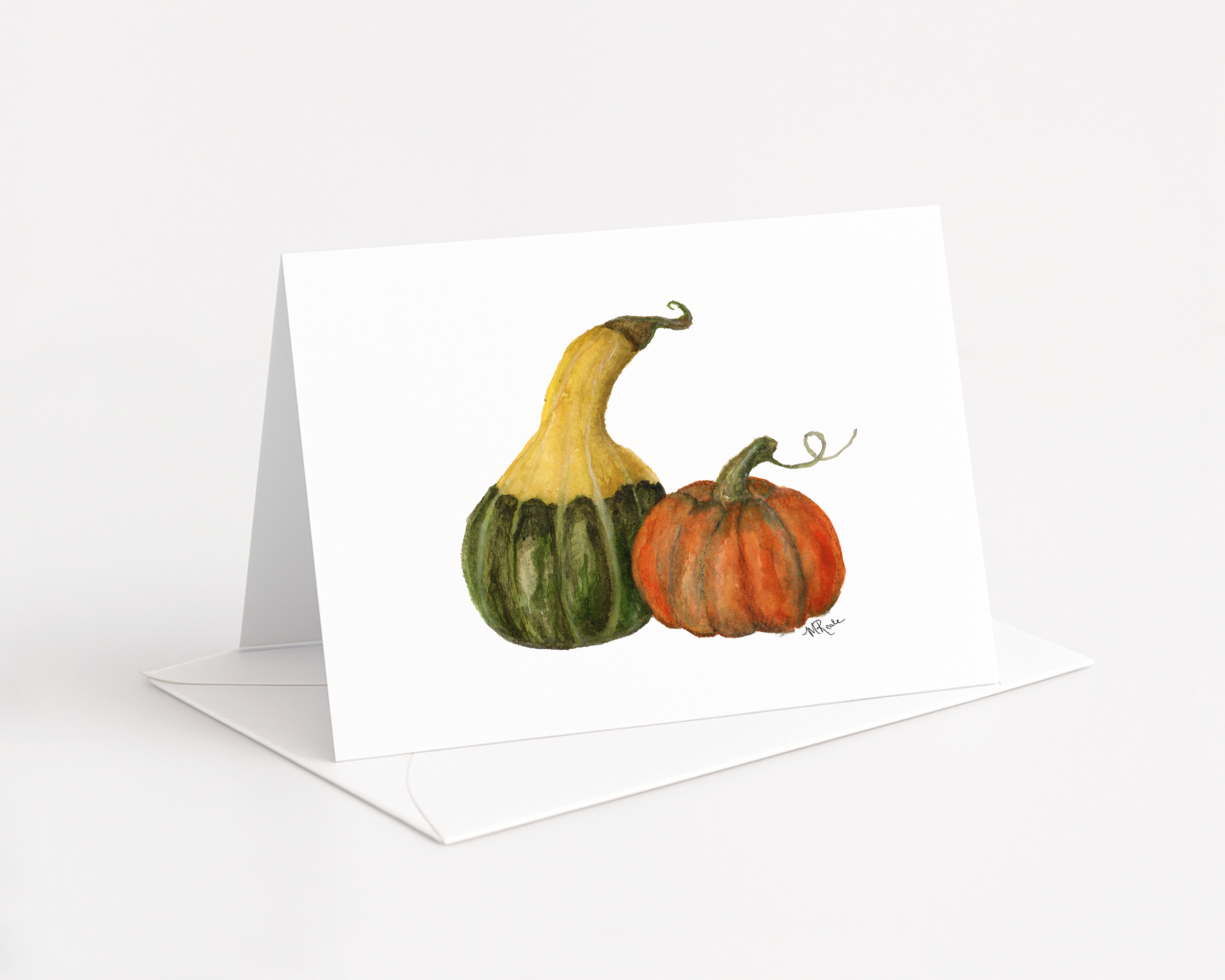 Watercolor painting of a gourd and two pumpkins on a white greeting card, propped on an envelope, against a white background.