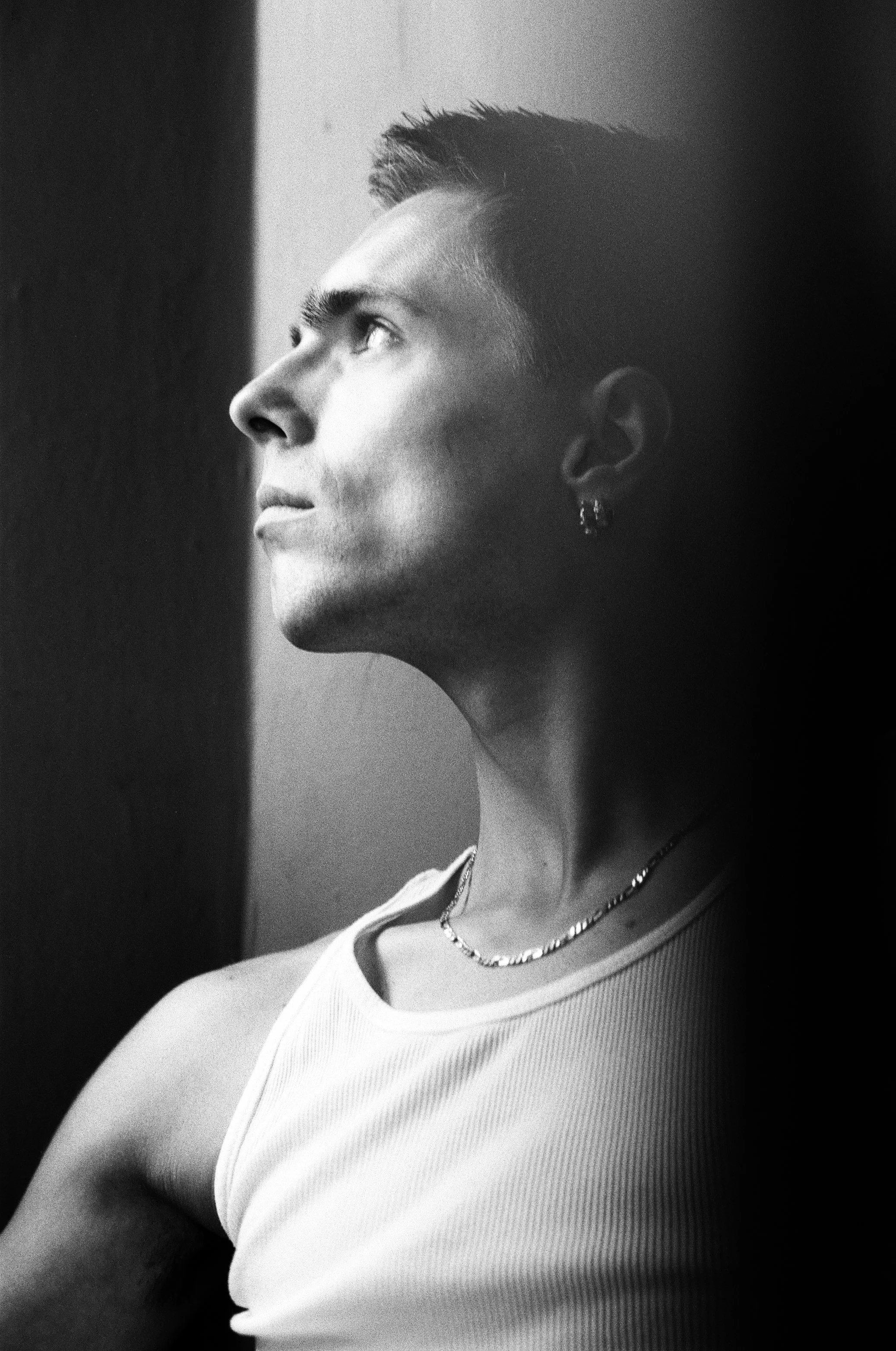 Black and white photo of a person with short hair looking to the left, wearing a sleeveless top, a necklace, and earrings.