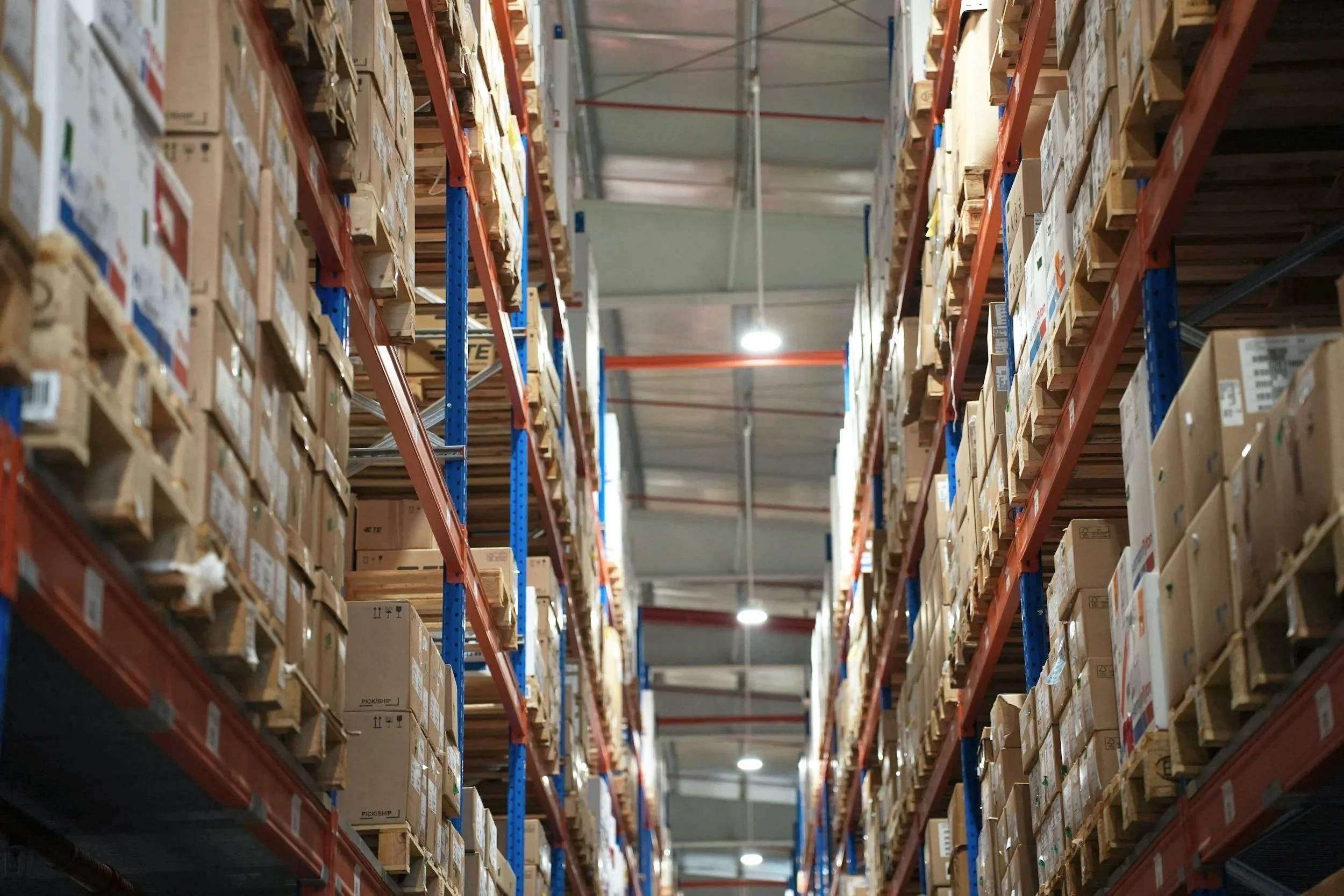 A warehouse aisle lined with tall shelves filled with cardboard boxes.