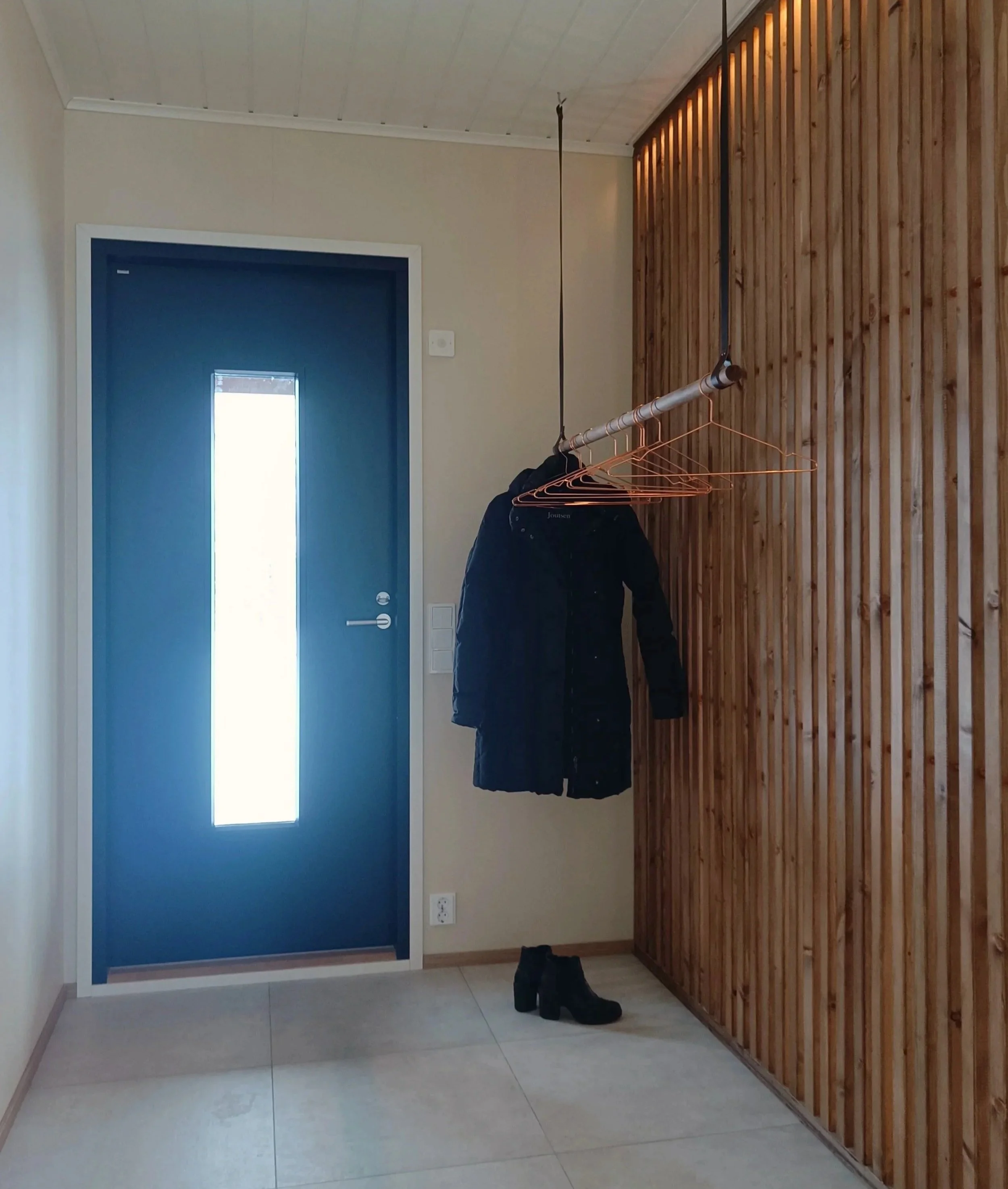 Koto sisäänkäynnissä, jossa on sininen ovi ja roikkumaan ripustettu vaatetanko, jossa on takki ja kenkä lattialla.