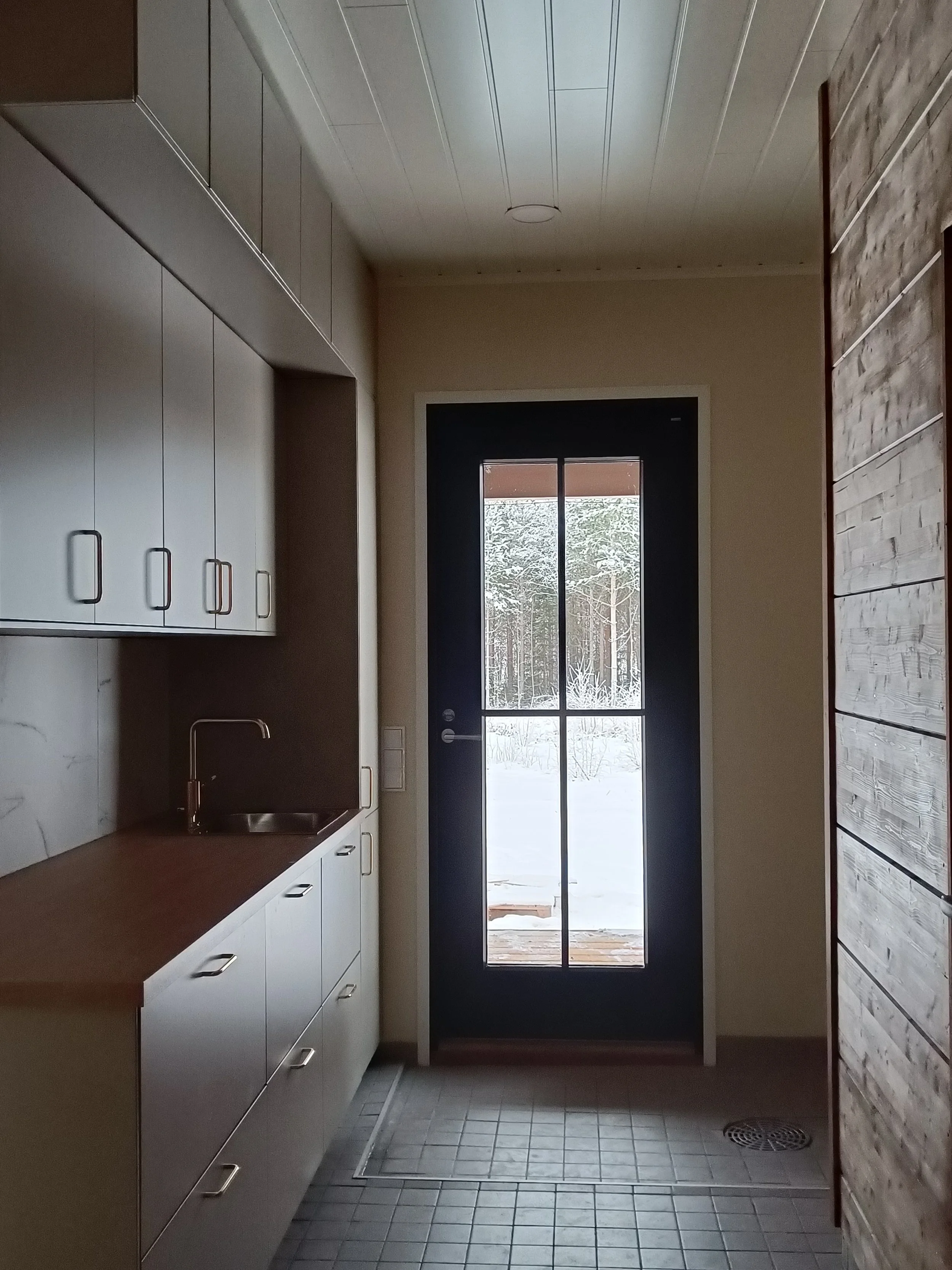 Keittiön sisäkuva, jossa valkoinen kaapisto ja pieni allas, takana lasiovi joka näkyy ulos lumiseen maisemaan.