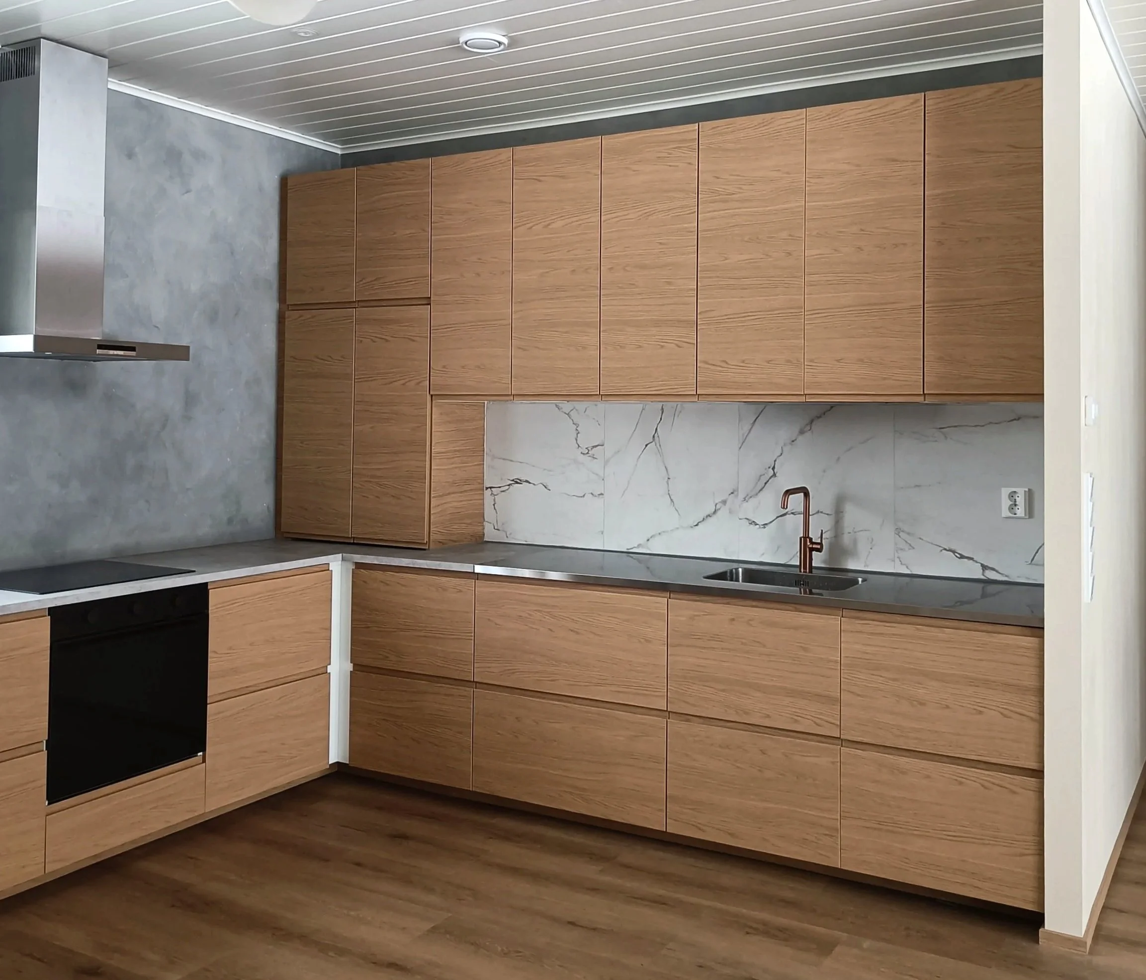 Keittiö, jossa puisten kaappien ja kivitasojen yhdistelmä, marmorialue seinällä ja puulattia.