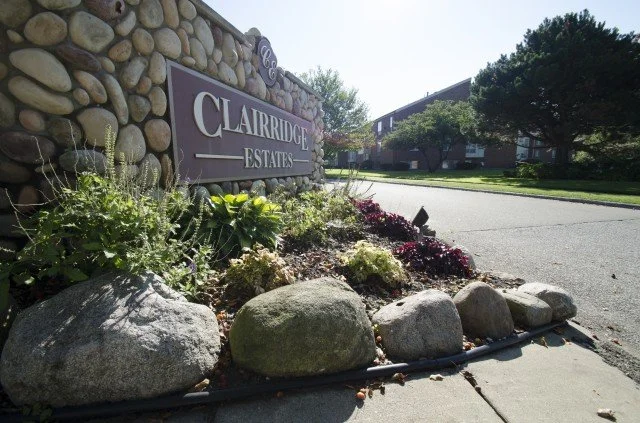 Sign for Heritage Grove Apartments made of rounded stones, surrounded by plants and rocks.