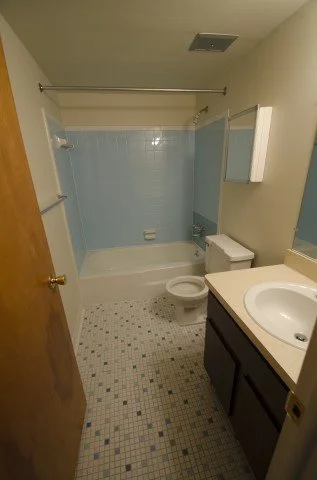 Small bathroom with a bathtub, shower curtain rod, toilet, and a dark wood vanity with a white sink, mirror, and medicine cabinet.
