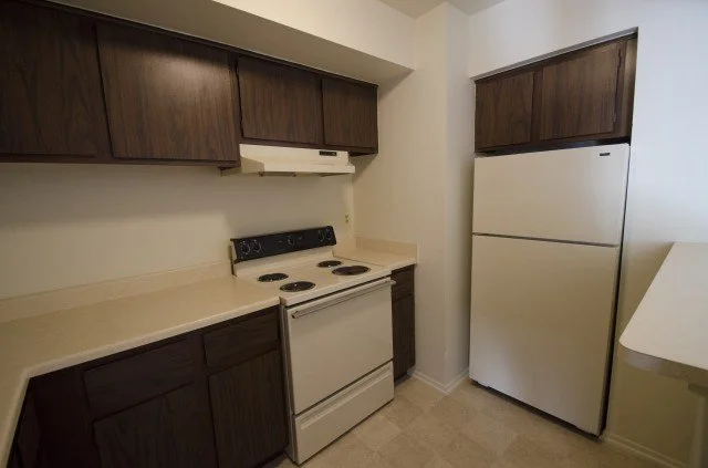 Small kitchen with dark wood cabinets, white refrigerator, white stove, and beige countertop.