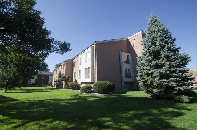 Apartment building with well-maintained lawn and trees under a clear blue sky in a residential area.