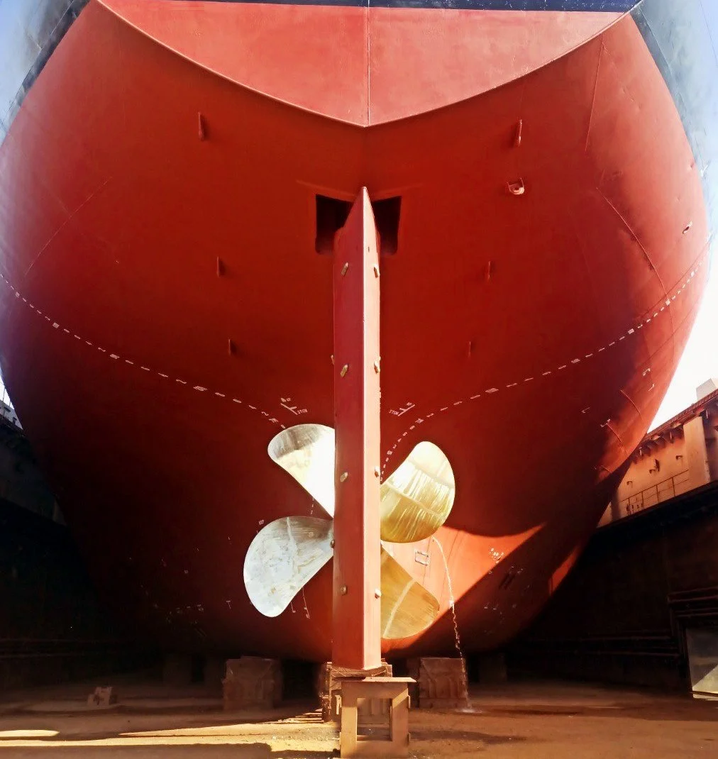 A large red ship hull viewed from underneath, showing the propeller at the bottom.
