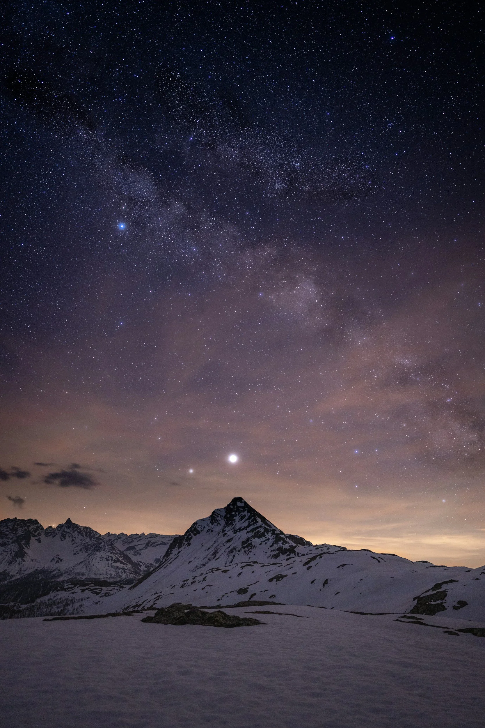 Snow-covered mountain under a starry night sky with planets visible.