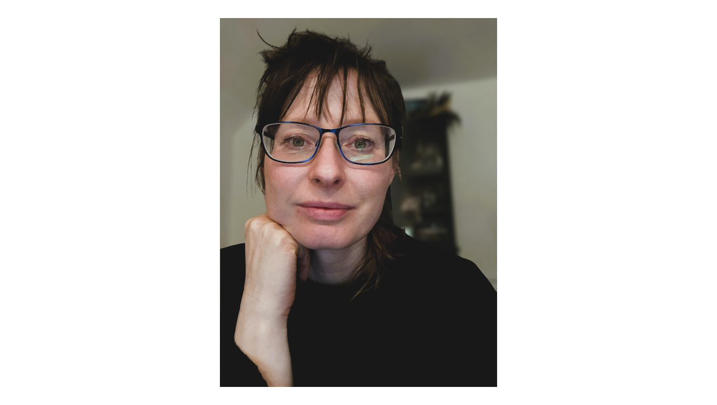 Close-up photo of a woman with short dark hair, glasses, and a slight smile, resting her chin on her hand in an indoor setting.