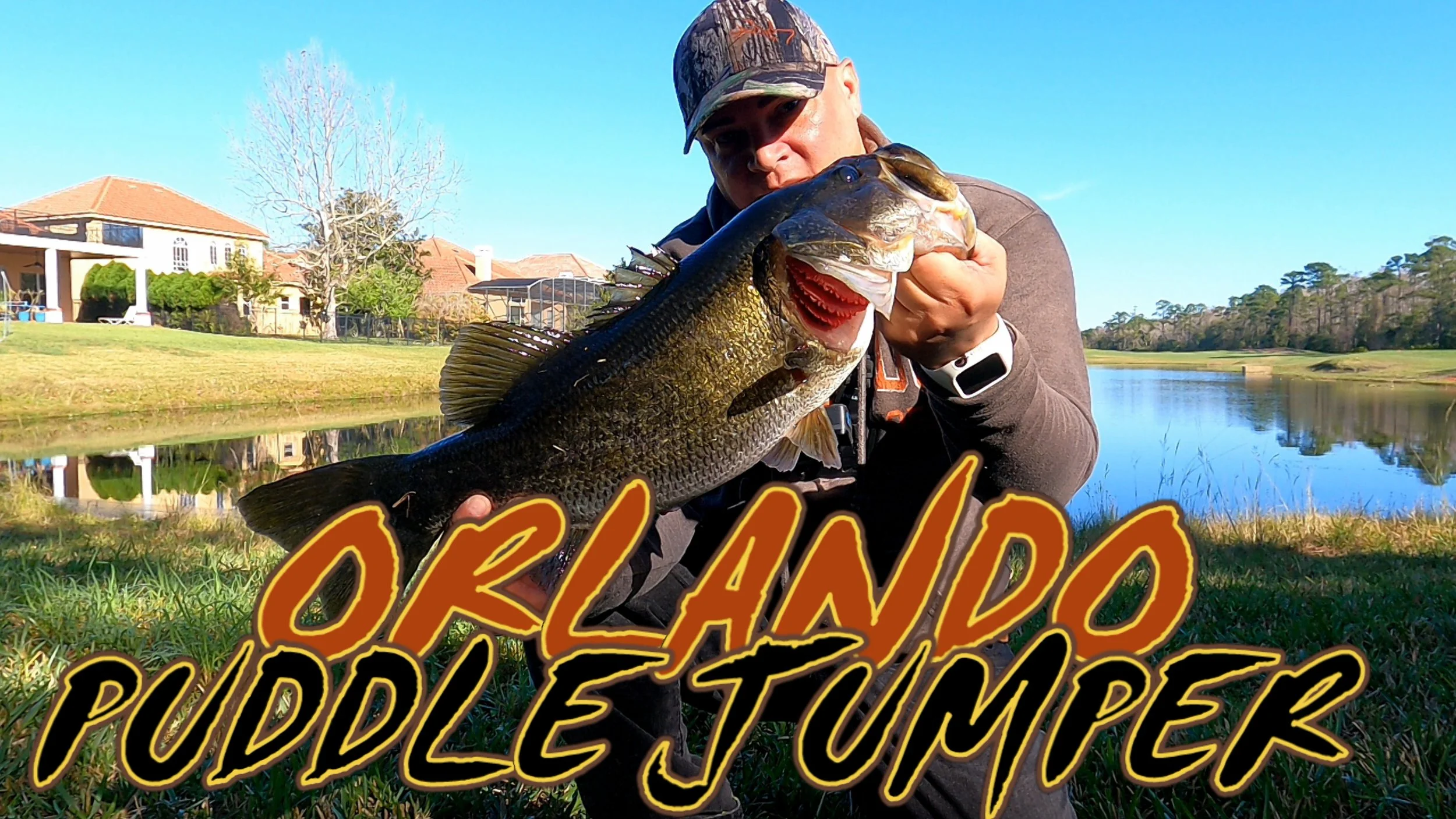 Man wearing a camouflage cap and gray hoodie holding a large bass fish near a pond with a house and trees in the background, with the text 'Oregon Puddle Jumper' overlaid.