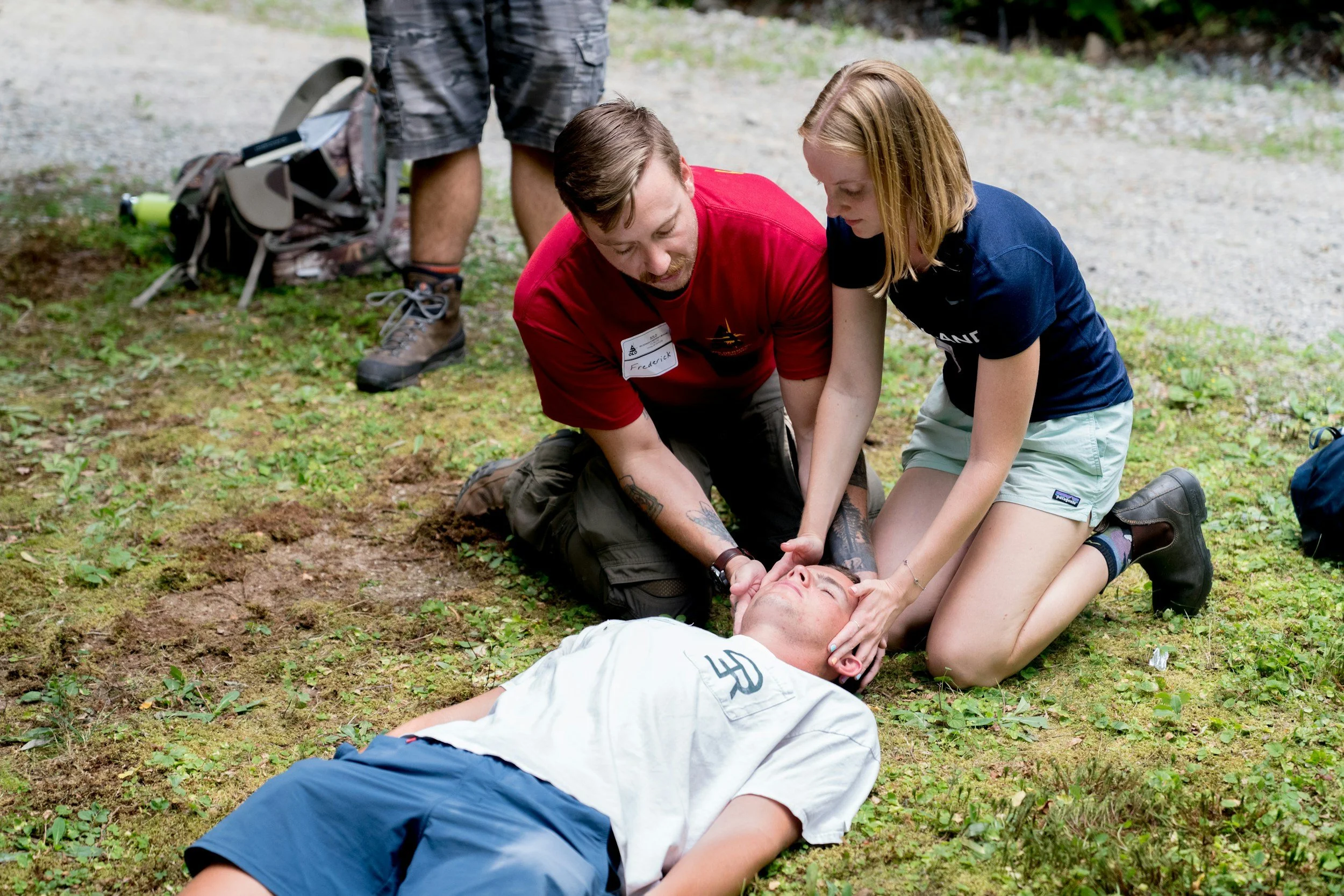 A group of people assisting a person lying on the ground outdoors, with one person performing CPR and others helping.
