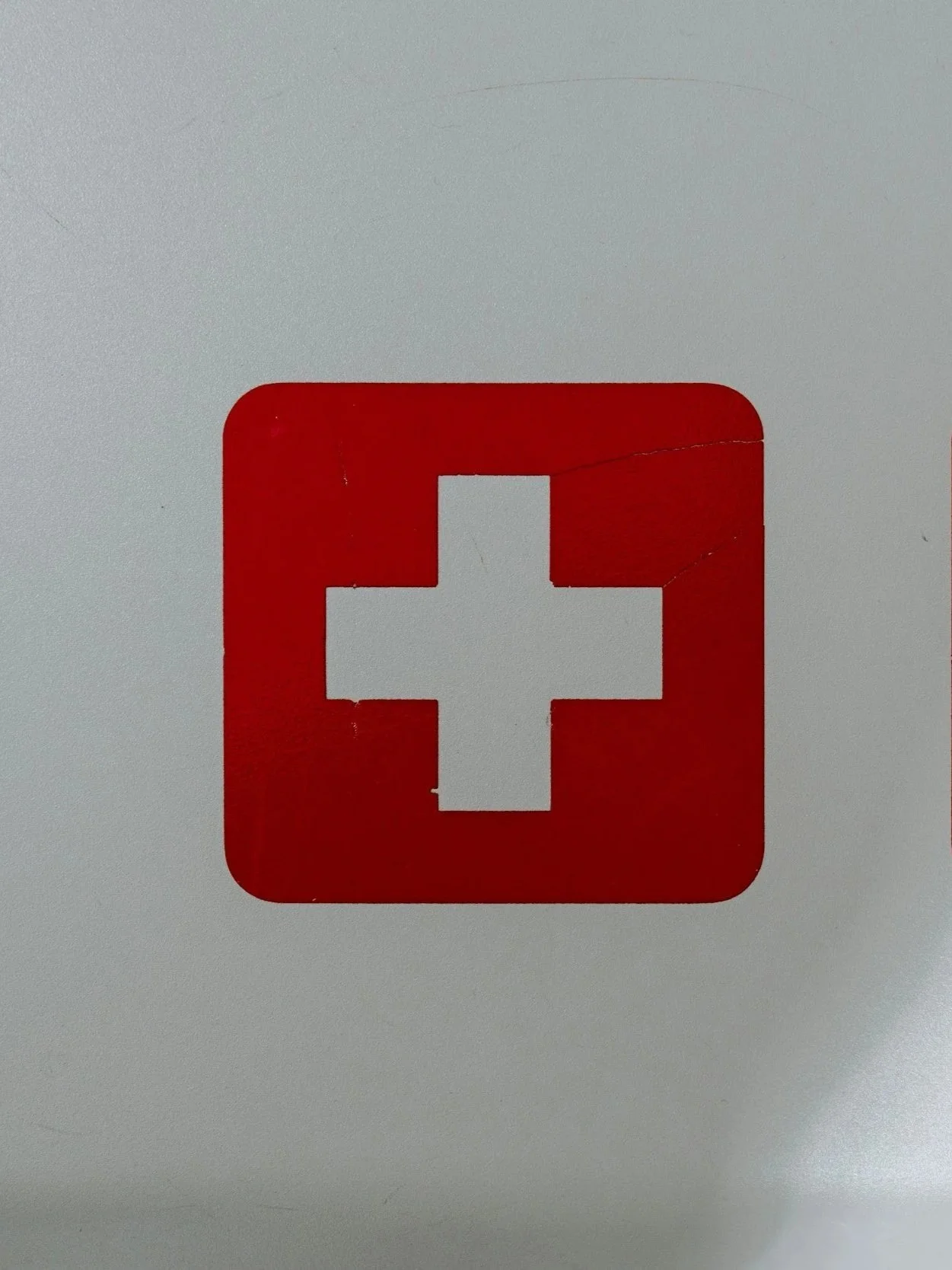 A white cross symbol inside a red square, indicating first aid or medical assistance.