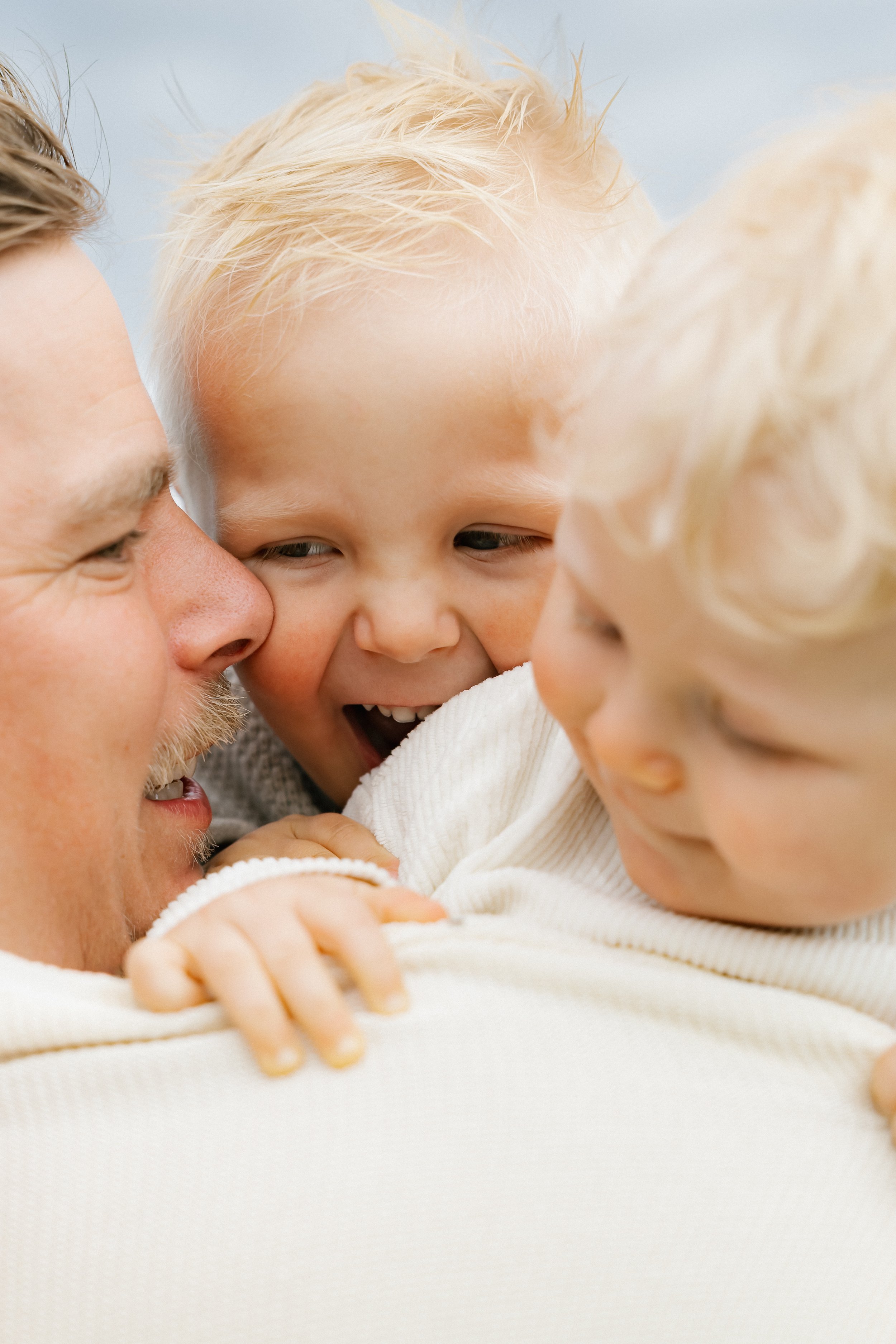 A man hugging two blonde young boys, all smiling and close together.