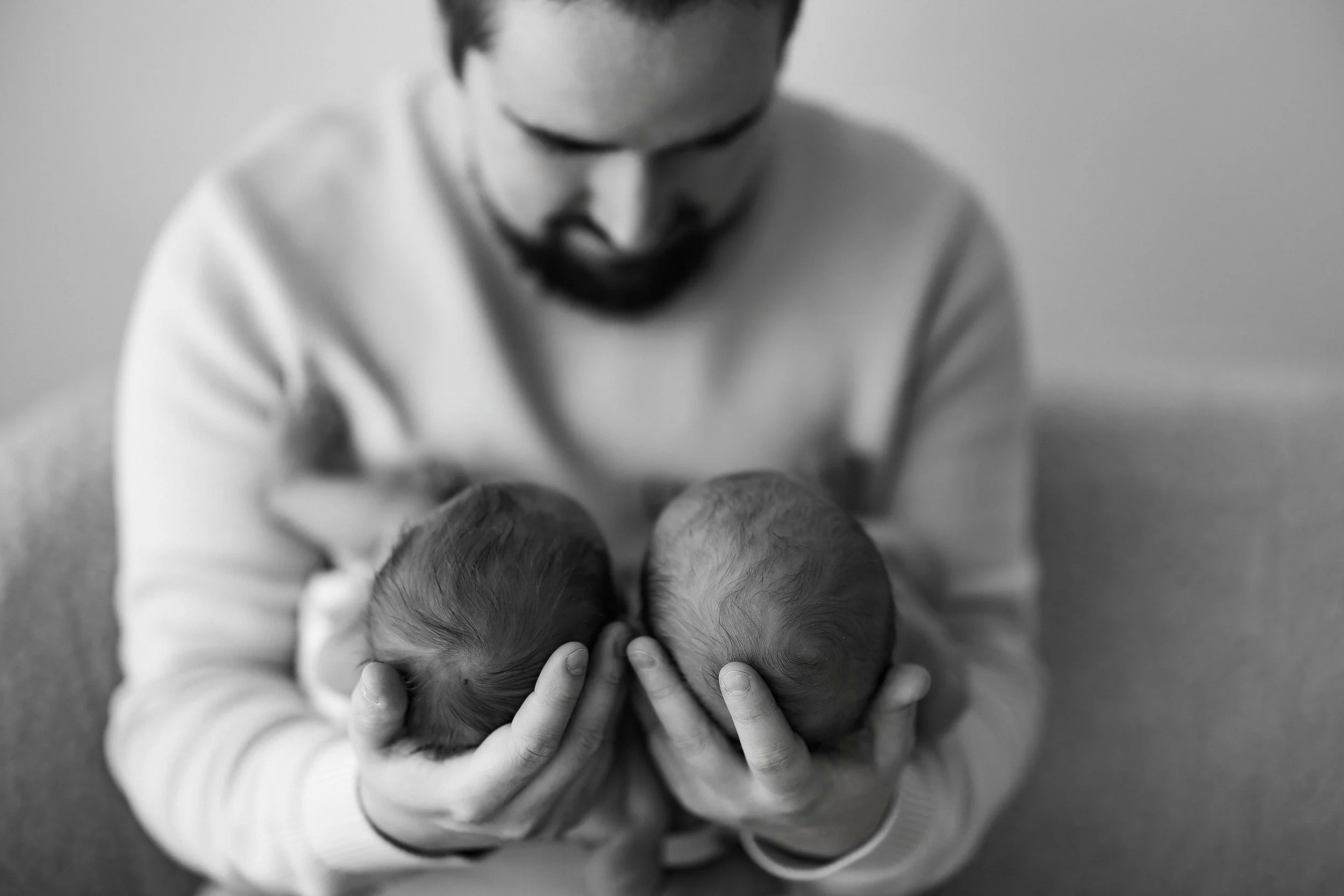 A man holding two newborn babies, one in each hand, as he looks down at them.
