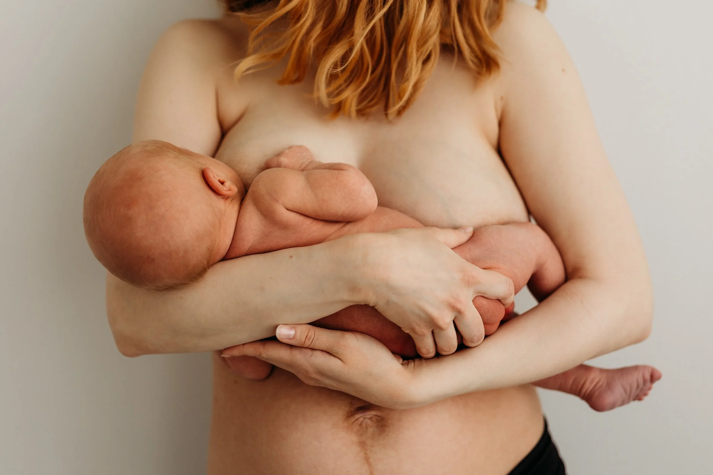 A woman with red hair holding a newborn baby in her arms, breastfeeding.