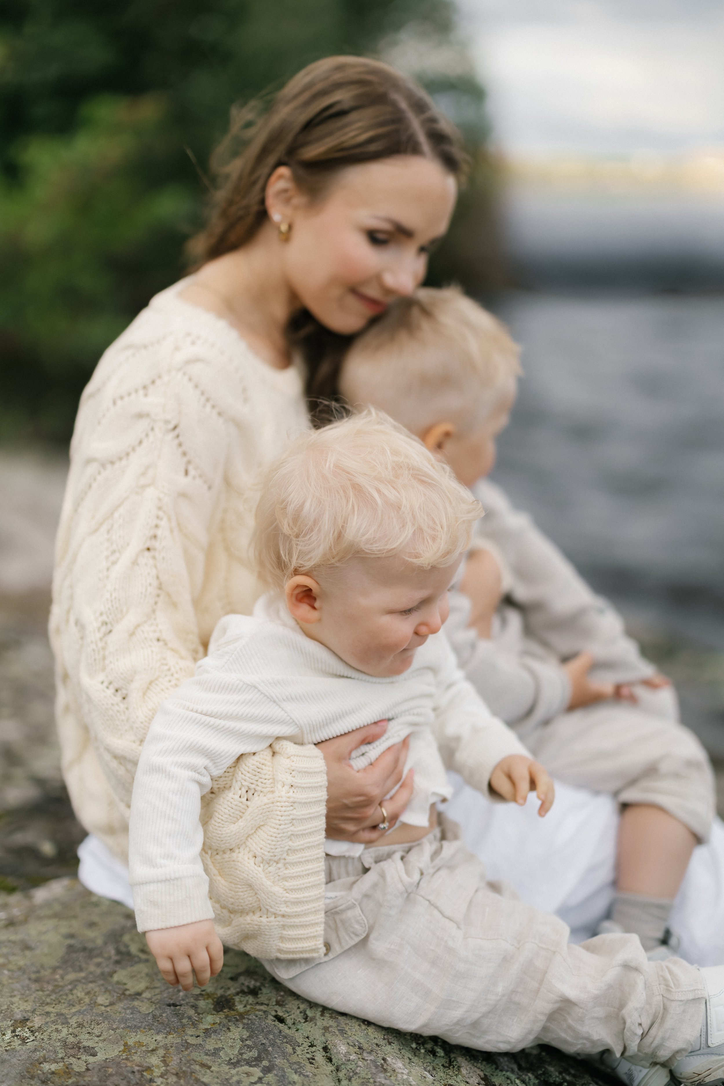 A woman with three young children by a body of water outdoors.