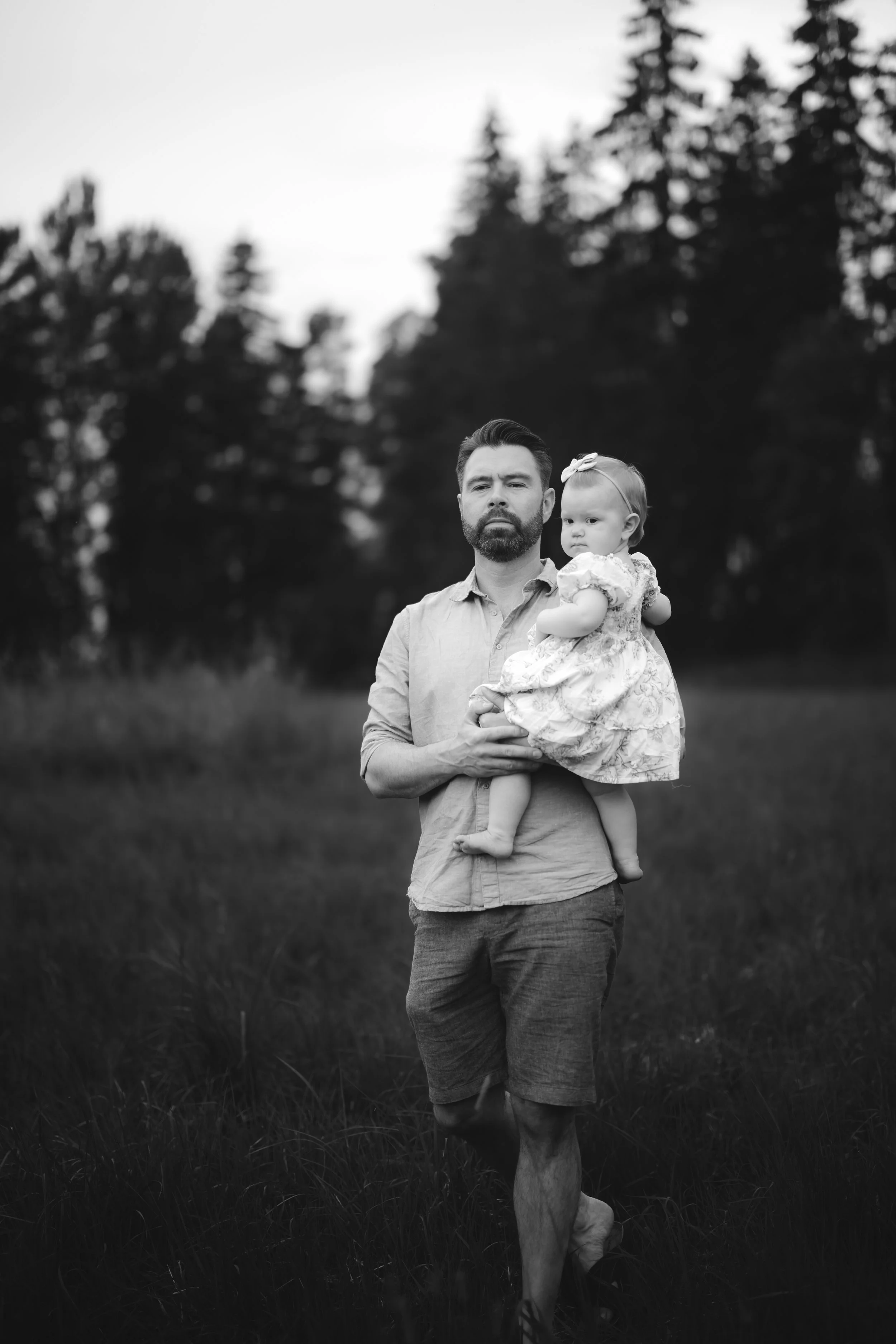 A man holding a young girl outdoors in a grassy field with trees in the background, in black and white.